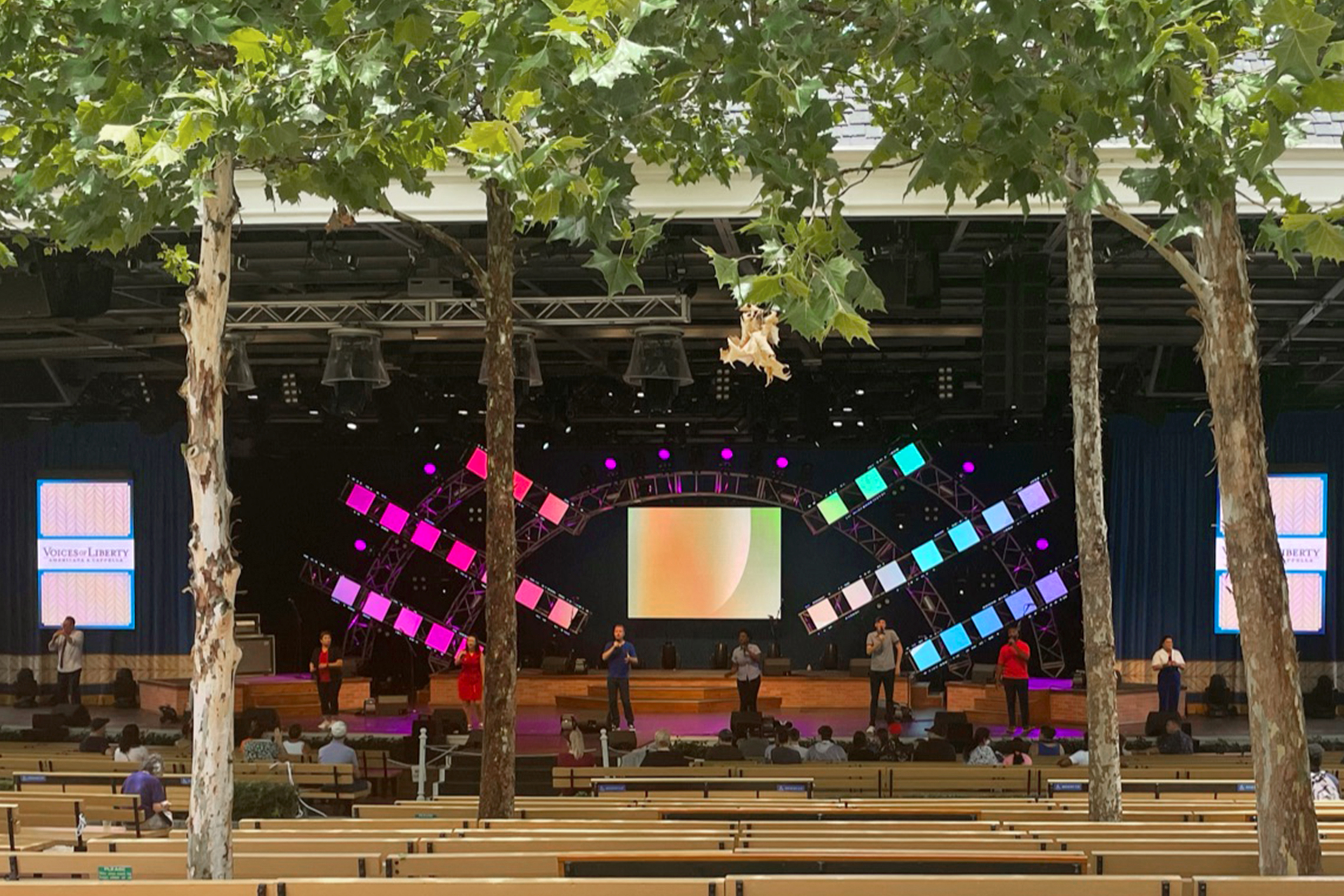 A group of performers stand in a line on a stage in front of LED screens at an outdoor theater.