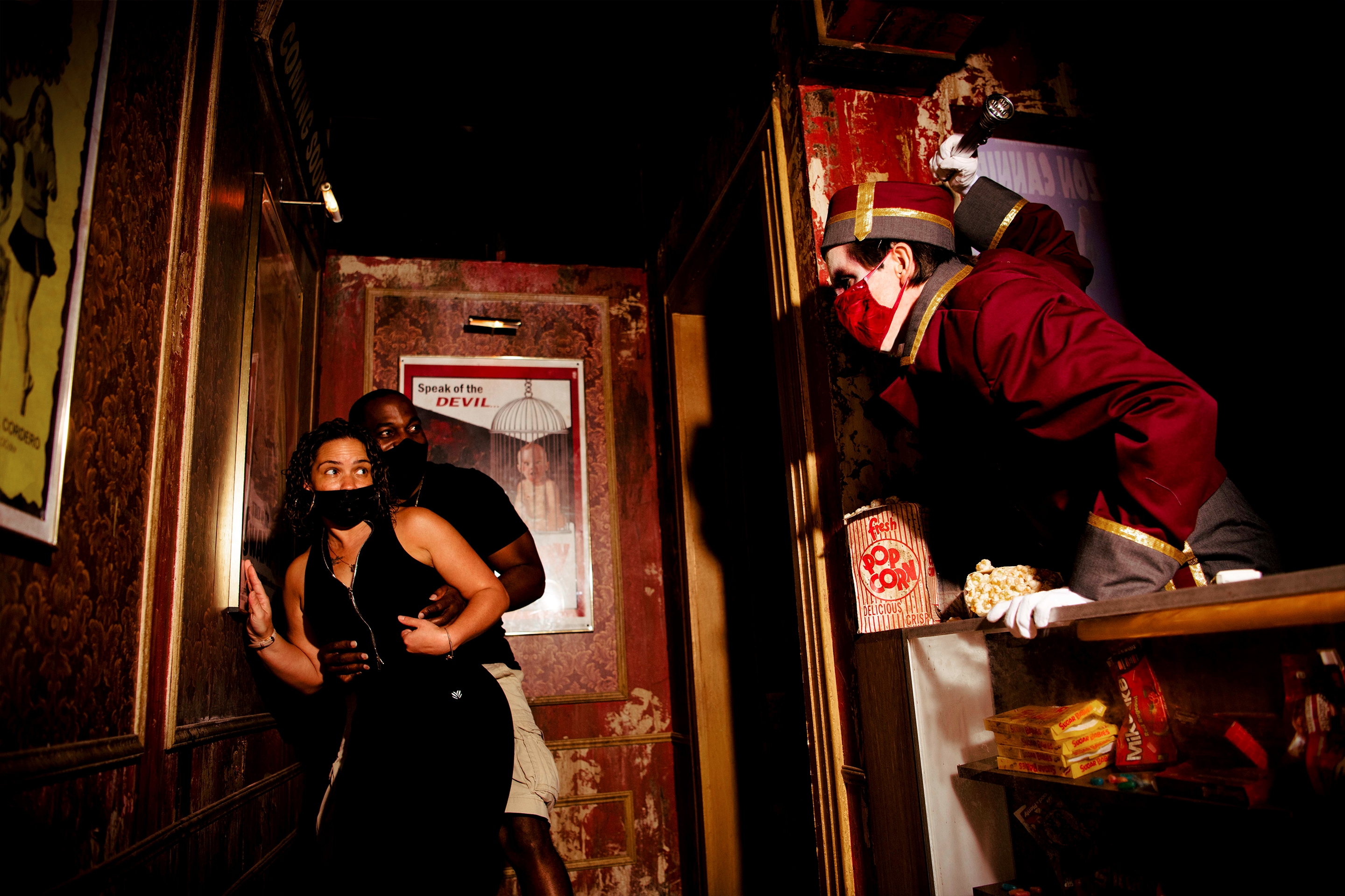 A man and woman hide from a horror nights performer in a Haunted House.