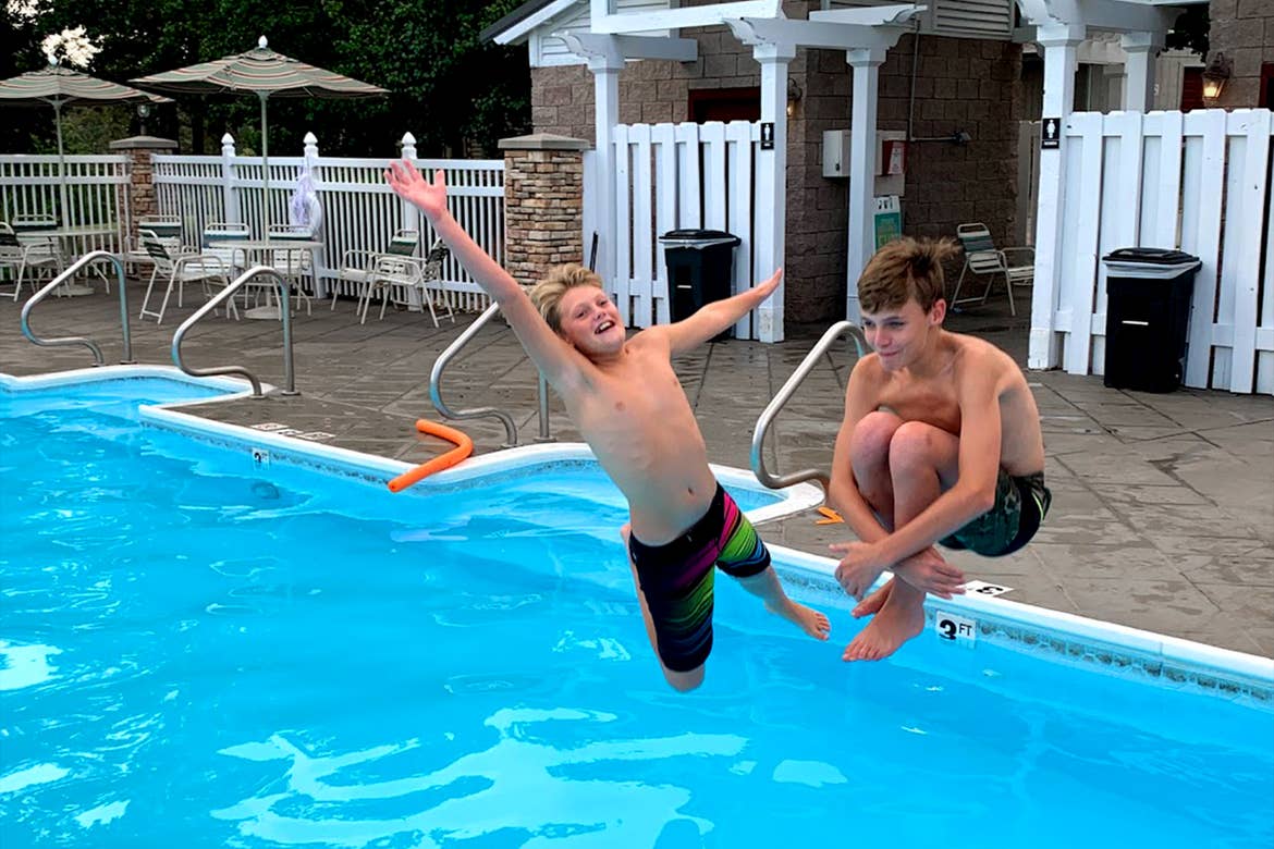 Two boys jump into an outdoor pool.
