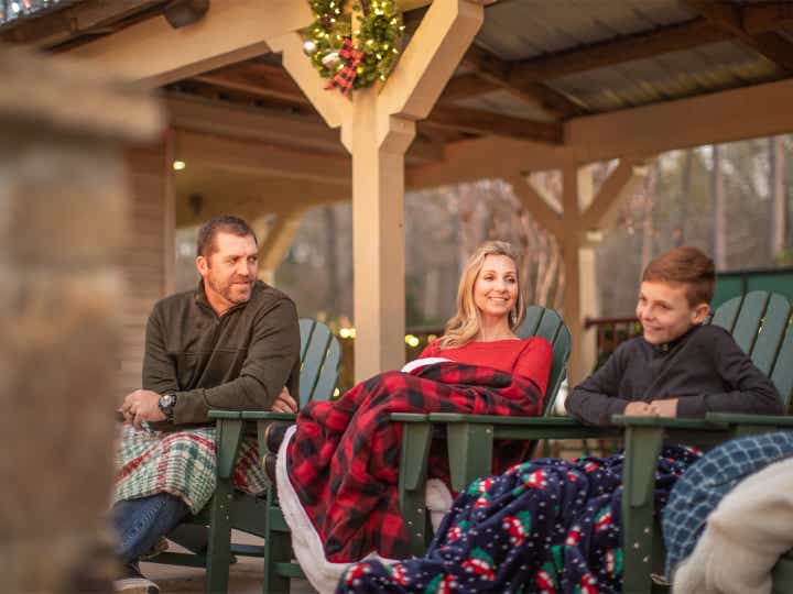 Family of three under blankets surrounded by festive holiday decor outdoors.
