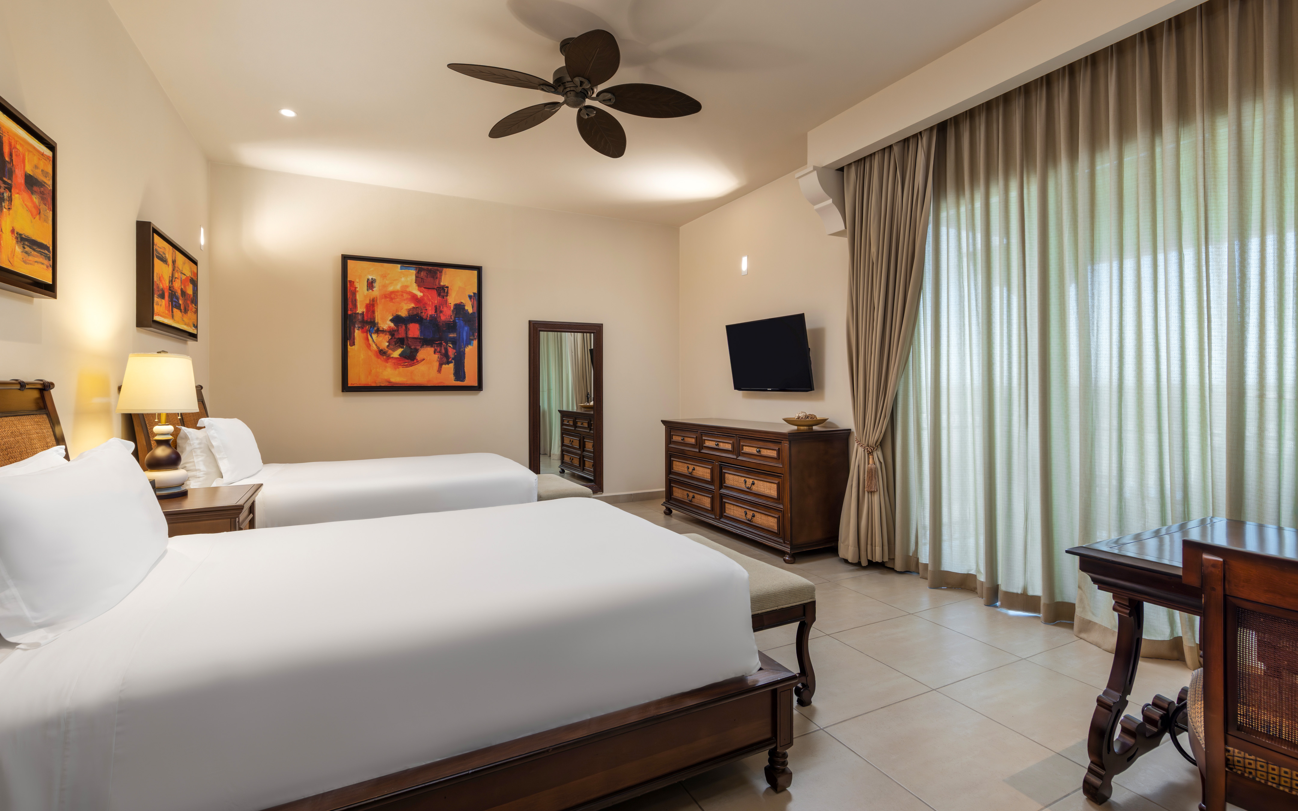 Suite bedroom with double beds, dresser, TV, and large window. 