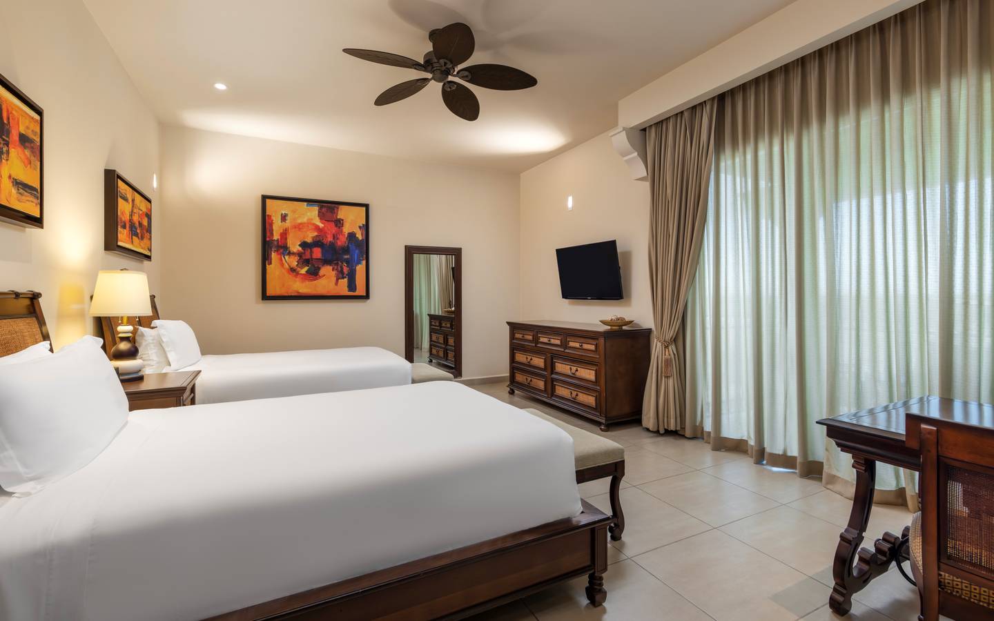 Suite bedroom with double beds, dresser, TV, and large window.