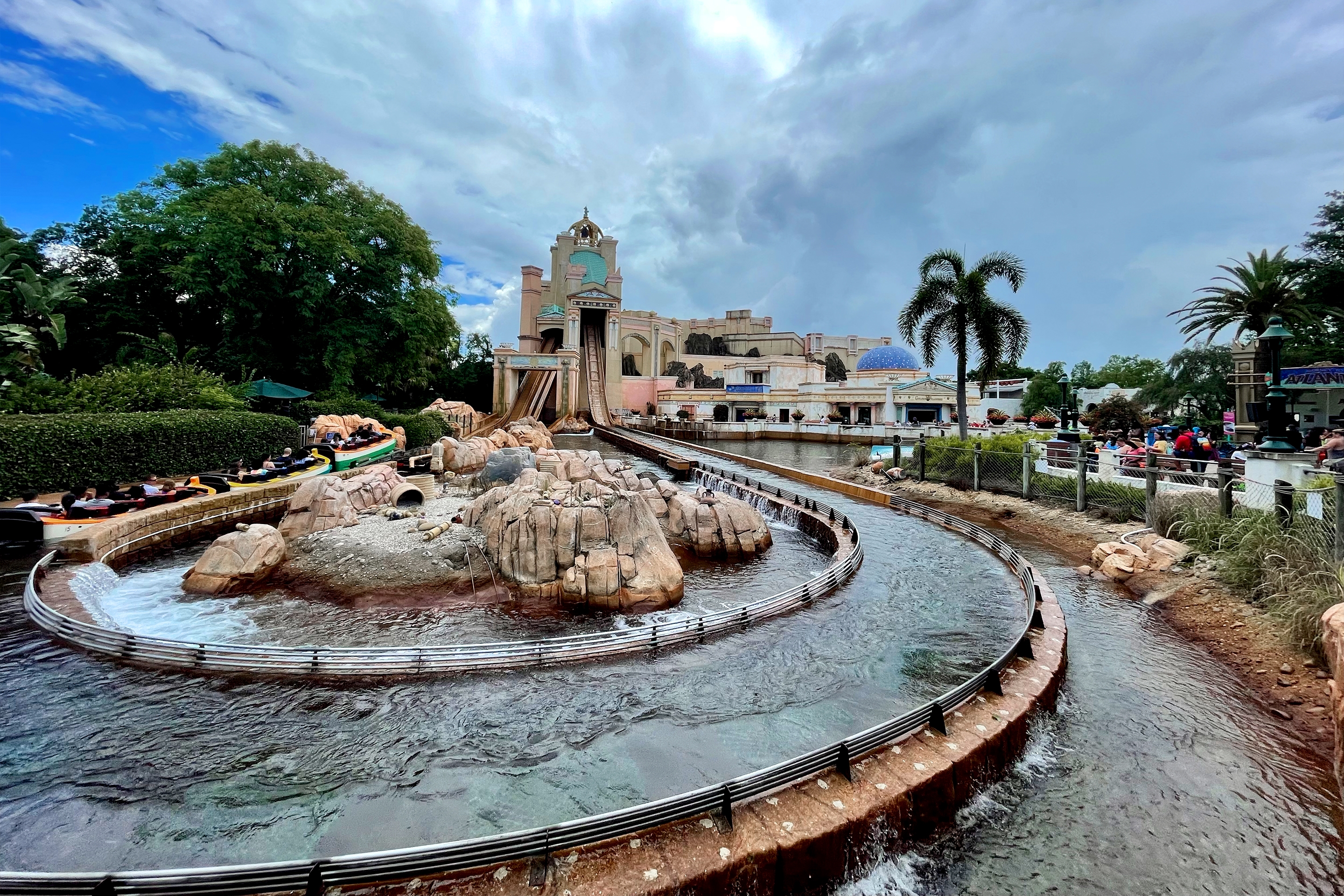 A water log ride exterior with a large drop stands surrounded by water near a guest walkway in SeaWorld Orlando.