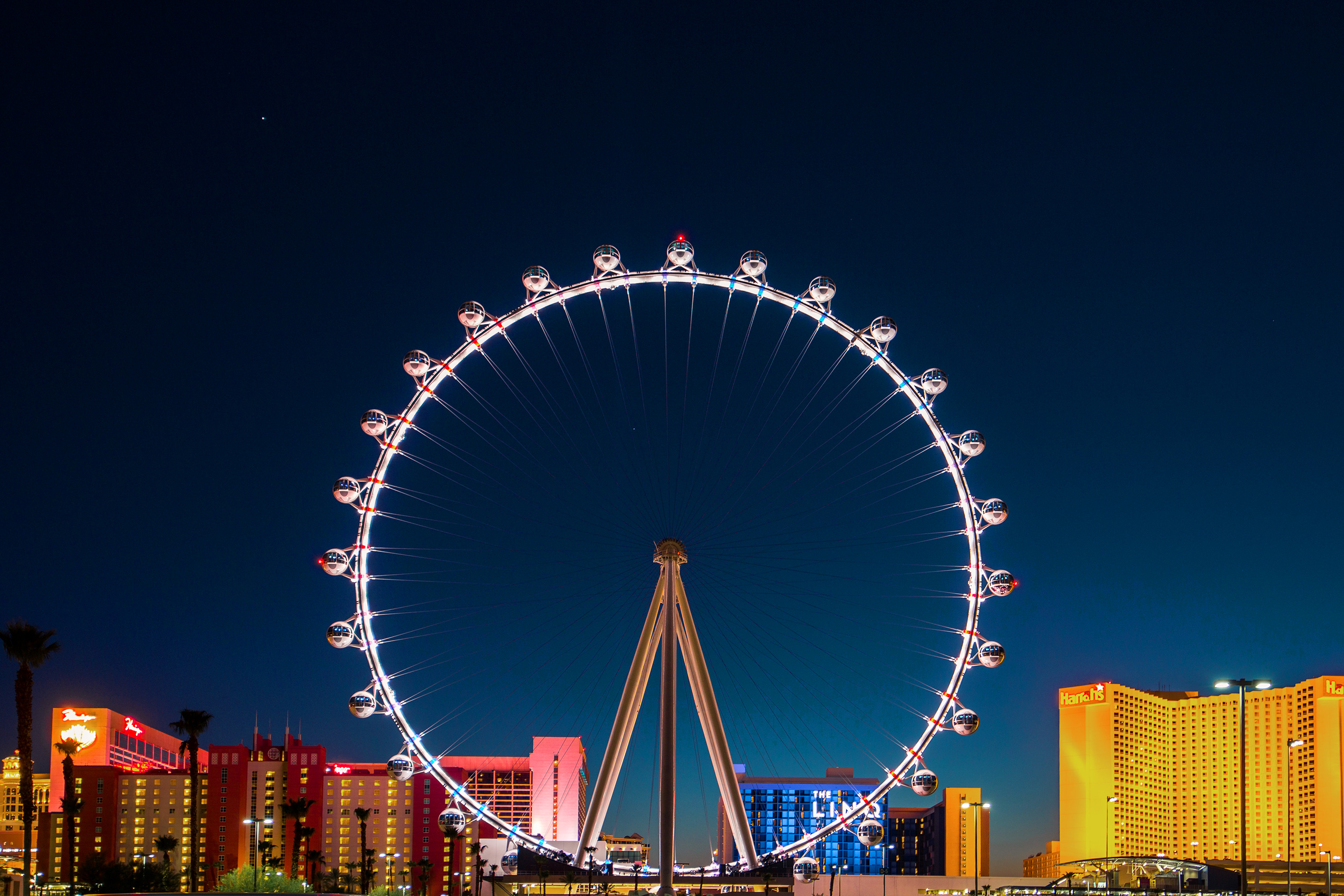 The 'High Roller' Ferris wheel stands illuminated in front of a dark blue night sky and surrounding buildings on The Las Vegas Strip.
