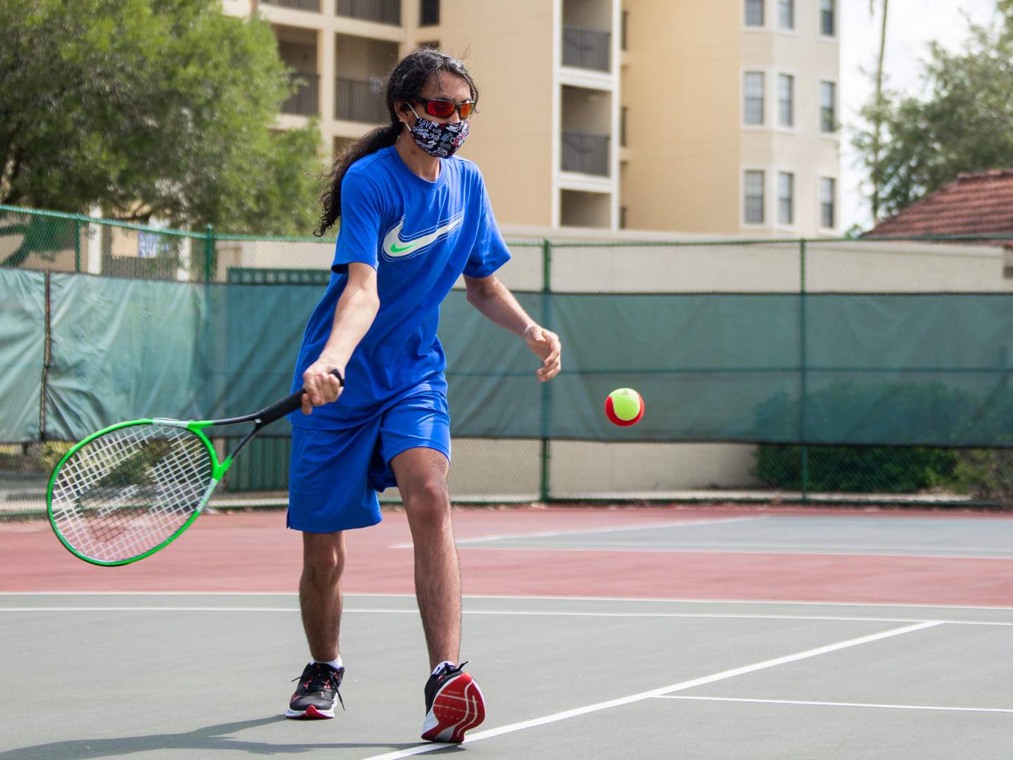 Special Olympic Athlete, Roan Luallen, plays tennis wearing a blue t-shirt and shorts with a safety mask and sunglasses on the courts of our Orange Lake Resort located in Orlando, Florida.