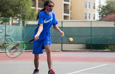 Special Olympic Athlete, Roan Luallen, plays tennis wearing a blue t-shirt and shorts with a safety mask and sunglasses on the courts of our Orange Lake Resort located in Orlando, Florida.