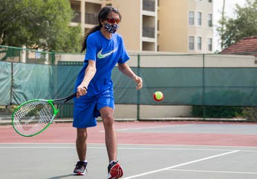 Special Olympic Athlete, Roan Luallen, plays tennis wearing a blue t-shirt and shorts with a safety mask and sunglasses on the courts of our Orange Lake Resort located in Orlando, Florida.