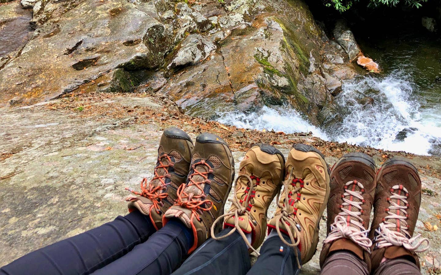 Featured Contributor, Jennifer C. Harmon (left) and her two girlfriends wear hiking boots as their feet sit near the top of a waterfall.