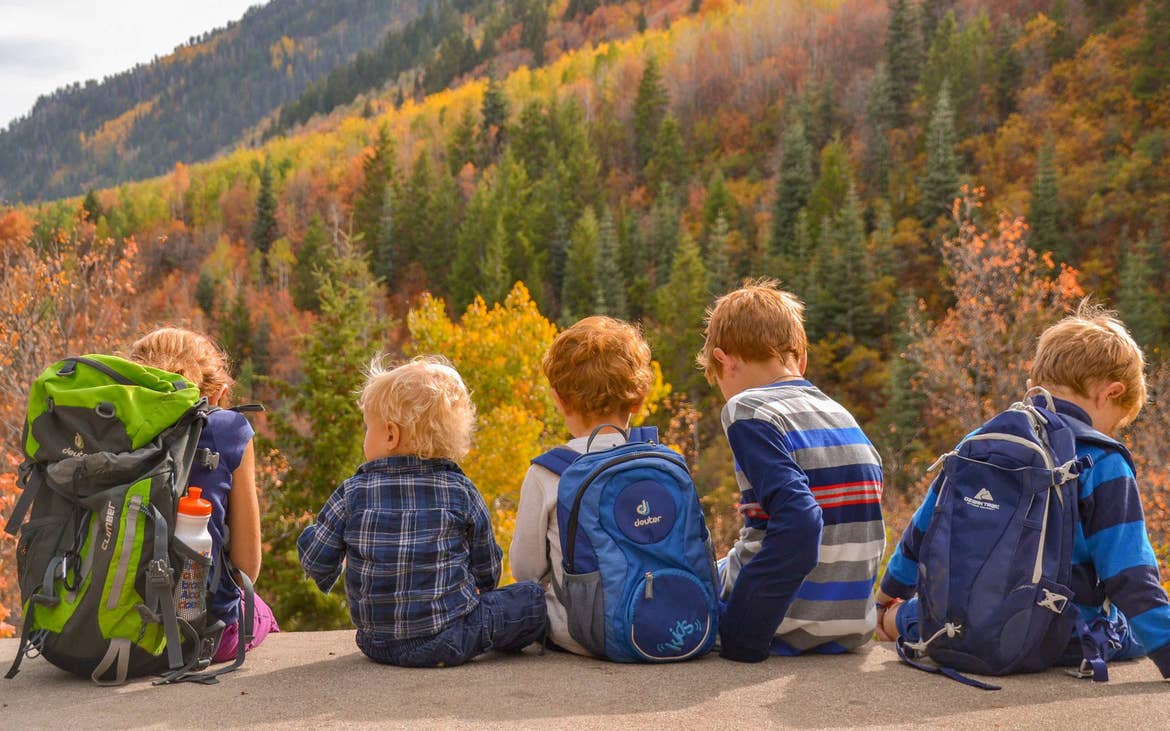 several children sit on a cliff overlooking fall foliage in the mountains.