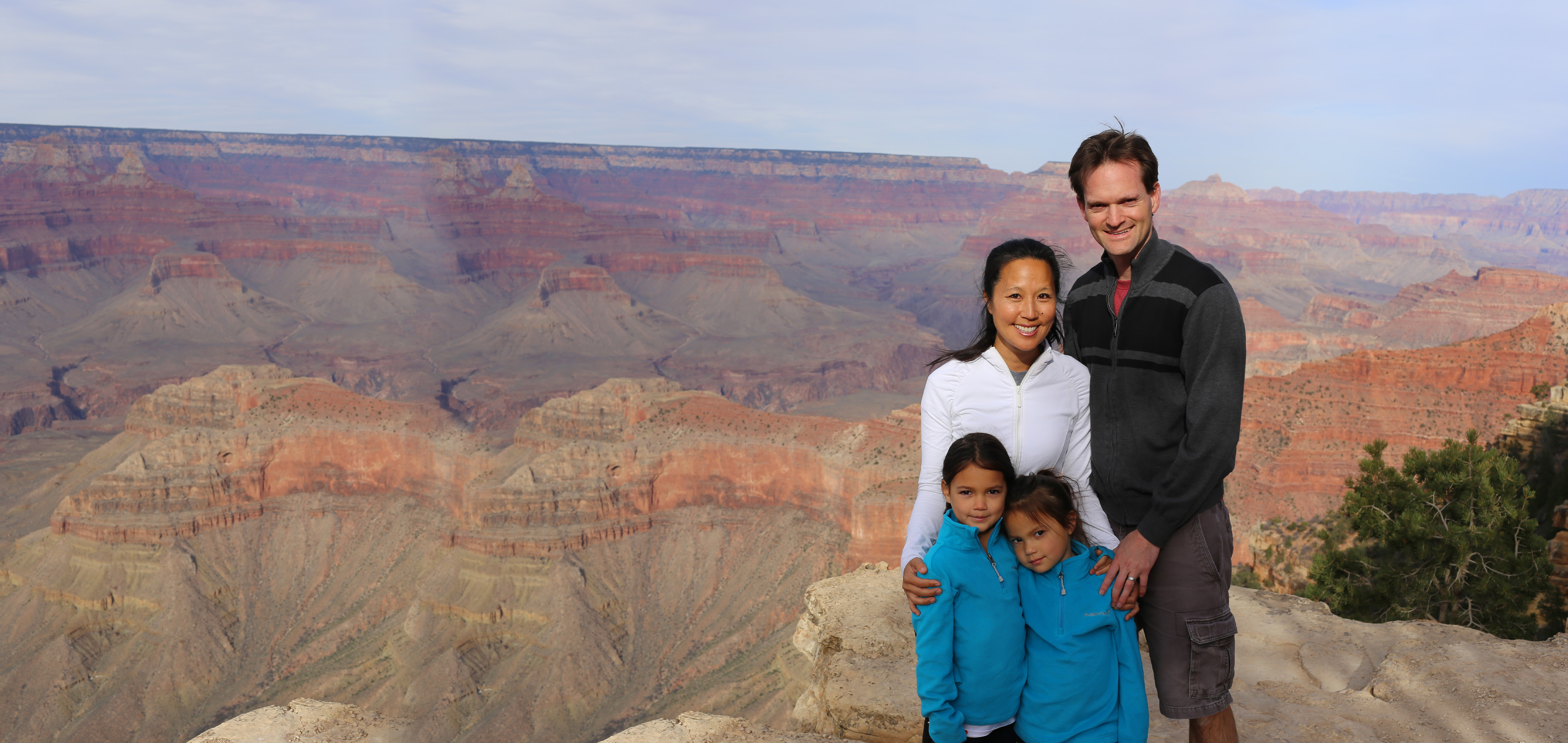 A woman, man and two young girls pose in front of the Grand Canyon wearing light jackets.