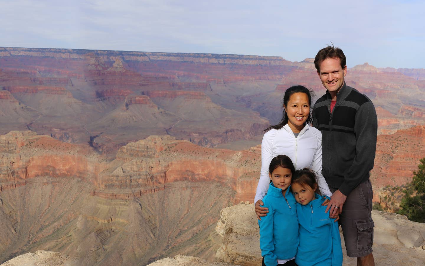 A woman, man and two young girls pose in front of the Grand Canyon wearing light jackets.