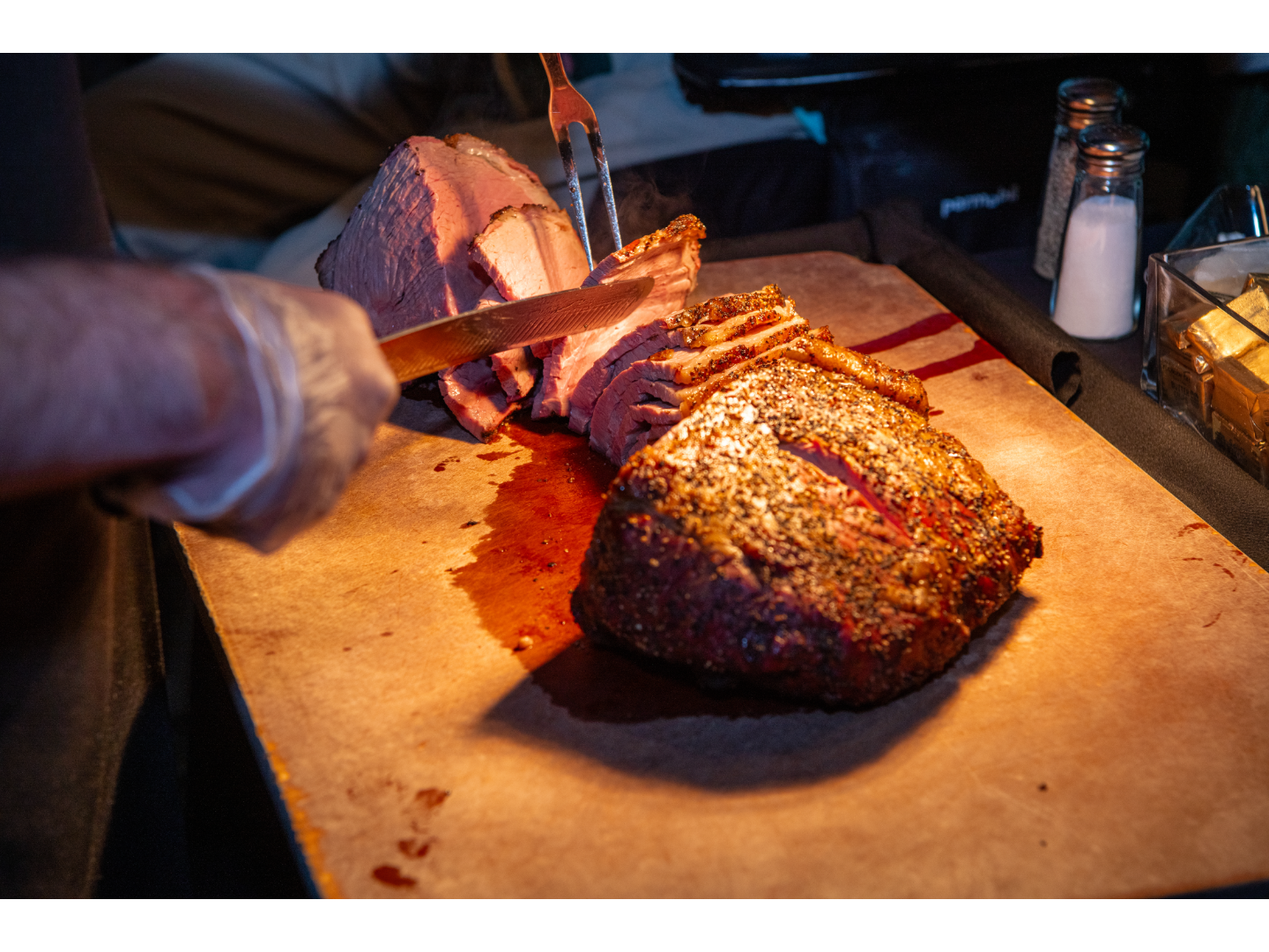 Chef slicing seasoned roast beef on cutting board with carving knife.