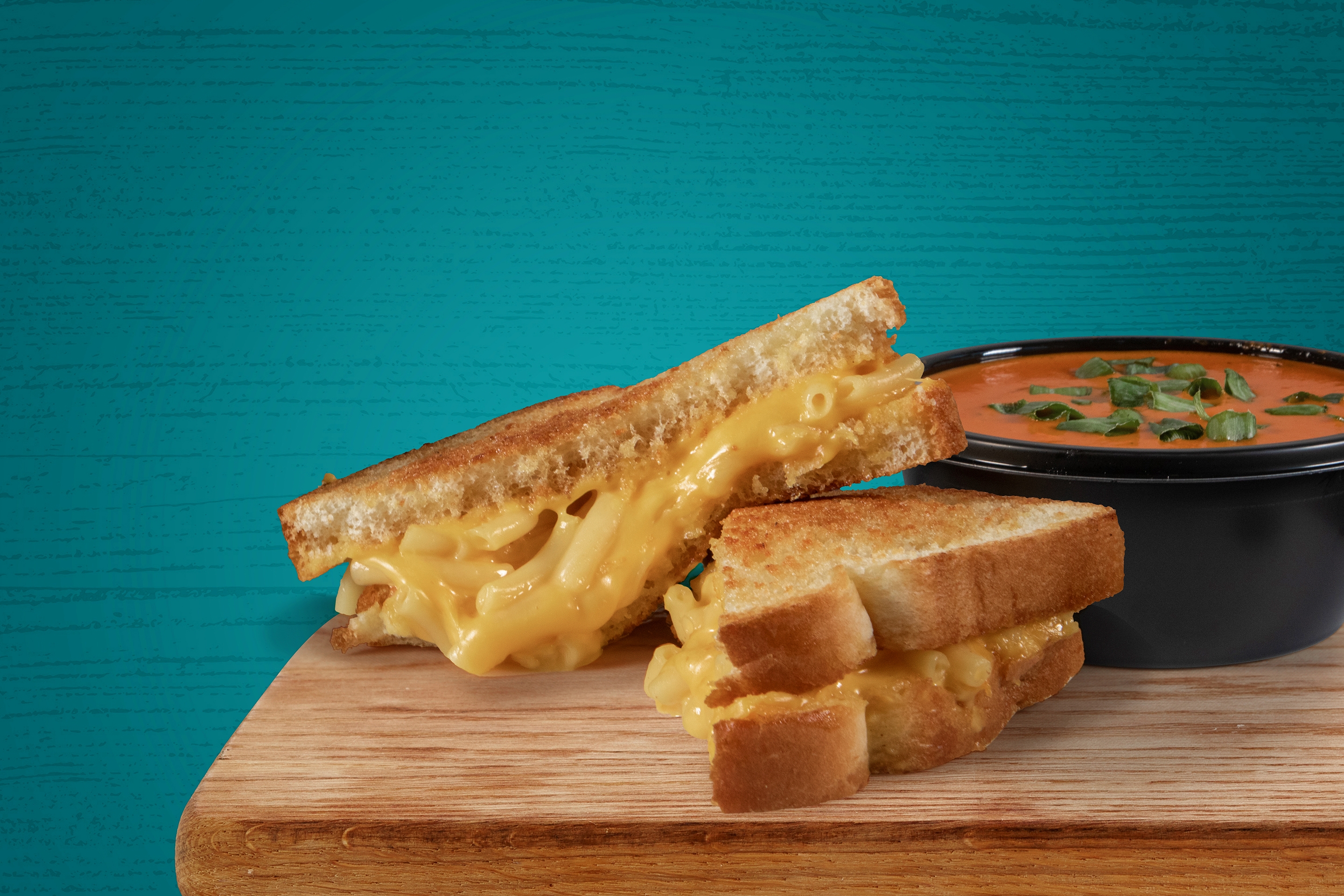 Grilled cheese on a plate near some tomato soup.