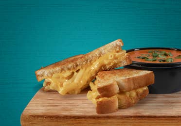 Grilled cheese on a plate near some tomato soup.