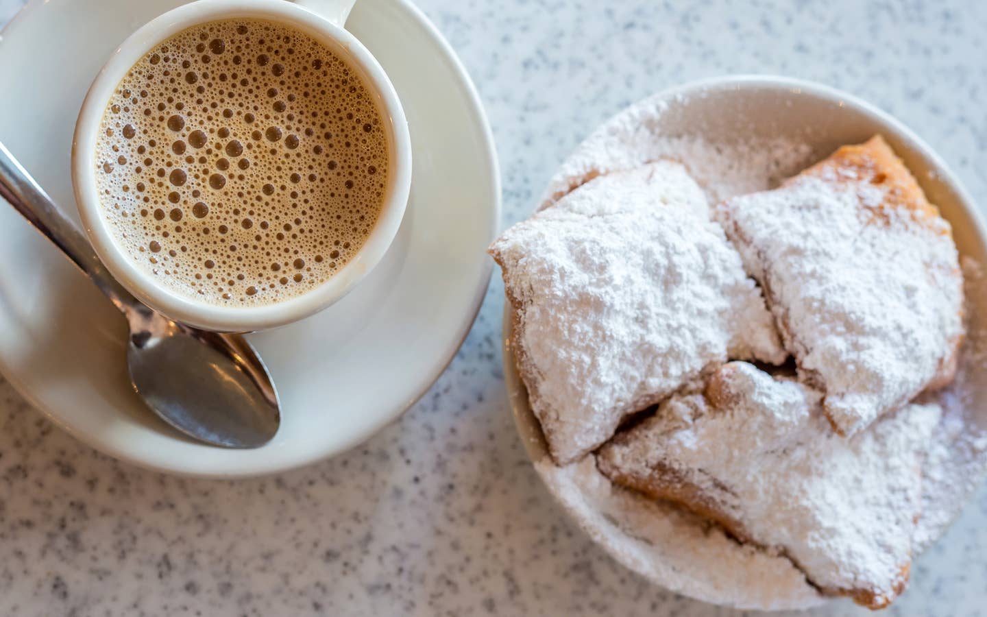 Beignets placed on a table with some coffee on white plates.