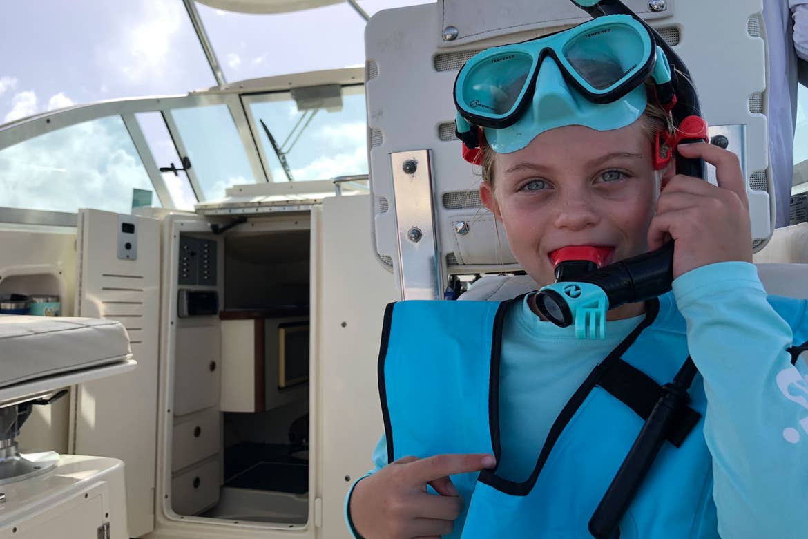 Featured Contributor, Chris Johnston's daughter, Kyndall, wears her Wacool snorkel vest and gear while sitting on a boat in the ocean.