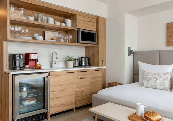 Contemporary hotel room showcasing cozy bed area and built-in kitchenette with microwave and beverage cooler.