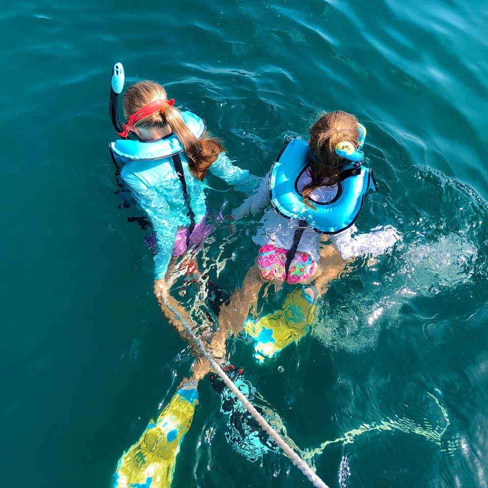 Featured Contributor, Chris Johnston's two daughters, Kyler (right) and Kyndall (left), wear multi-colored snorkel gear while holding onto a rope in the ocean.