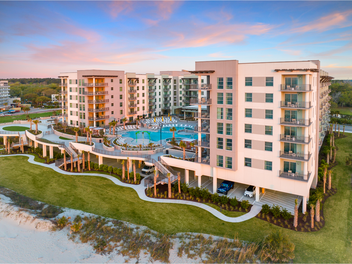 Modern beachfront resort with pool and balconies at sunset.