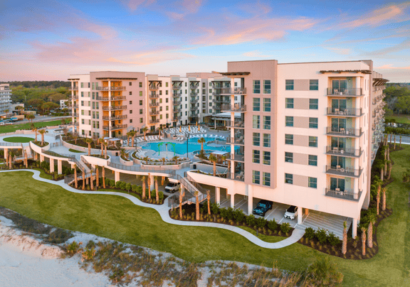 Modern beachfront resort with pool and balconies at sunset.