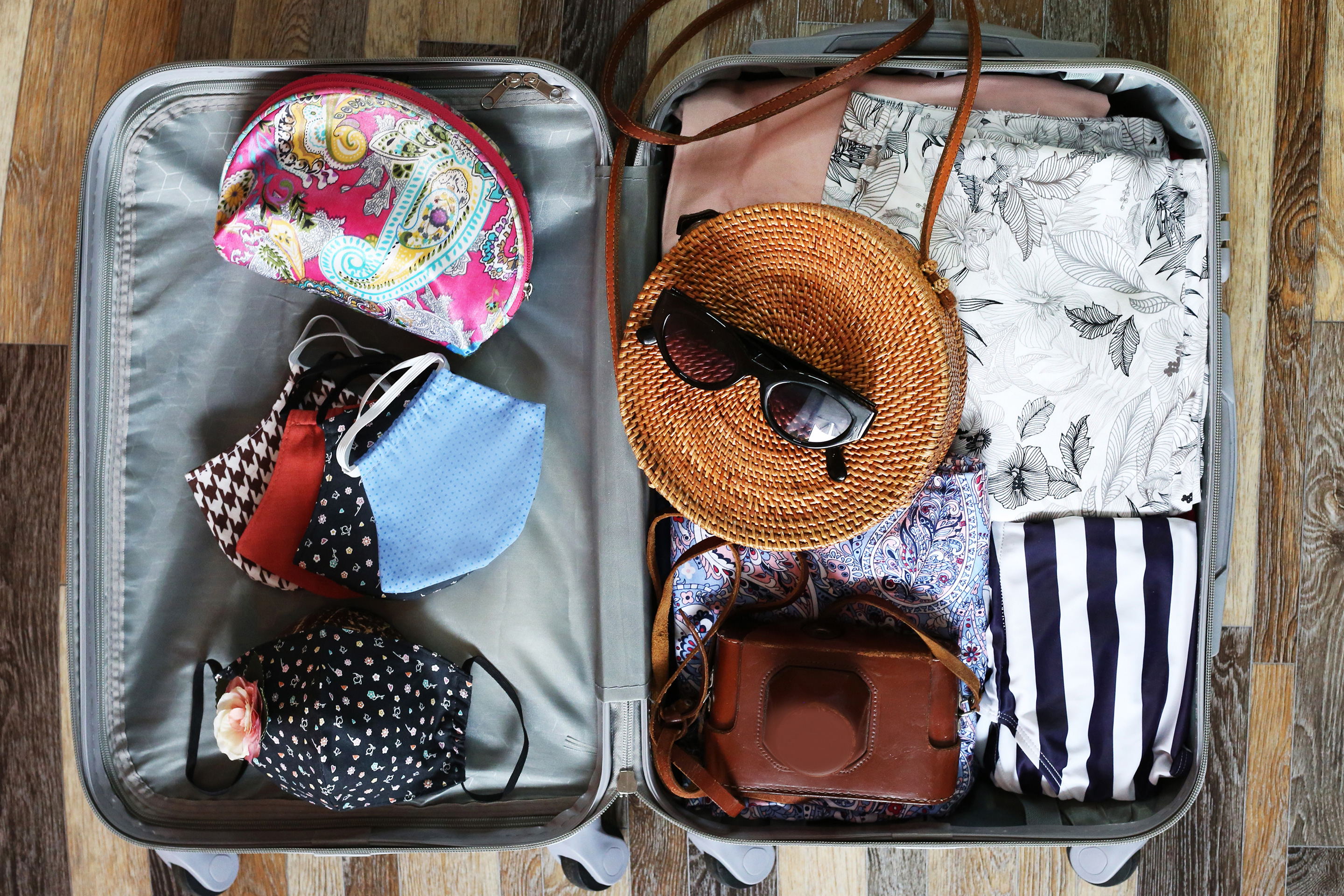 An open suitcase containing women's clothing, masks, bags, and accessories.