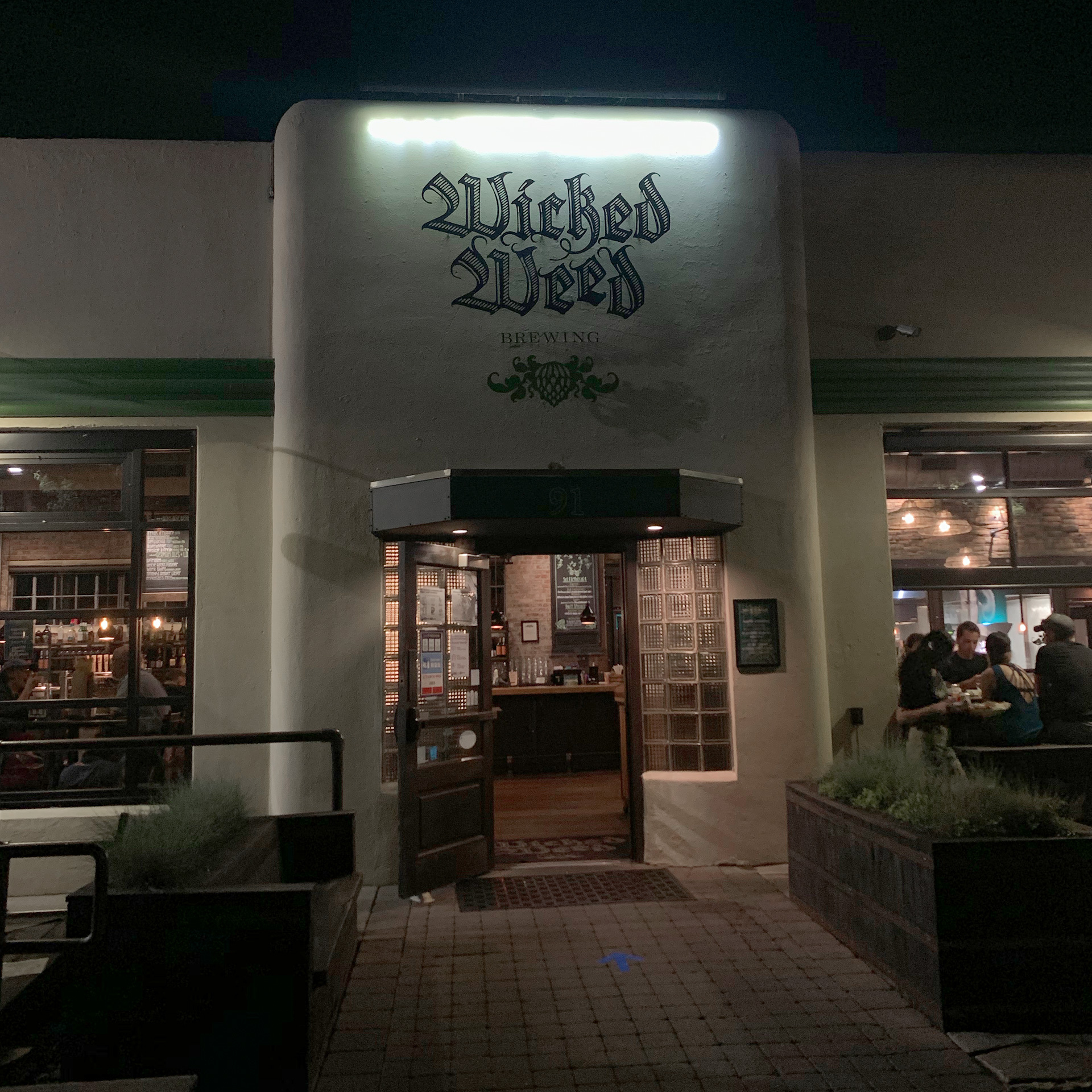 Brewery exterior with stucco white walls and painted sign that reads, 'Wicked Weed' in green.