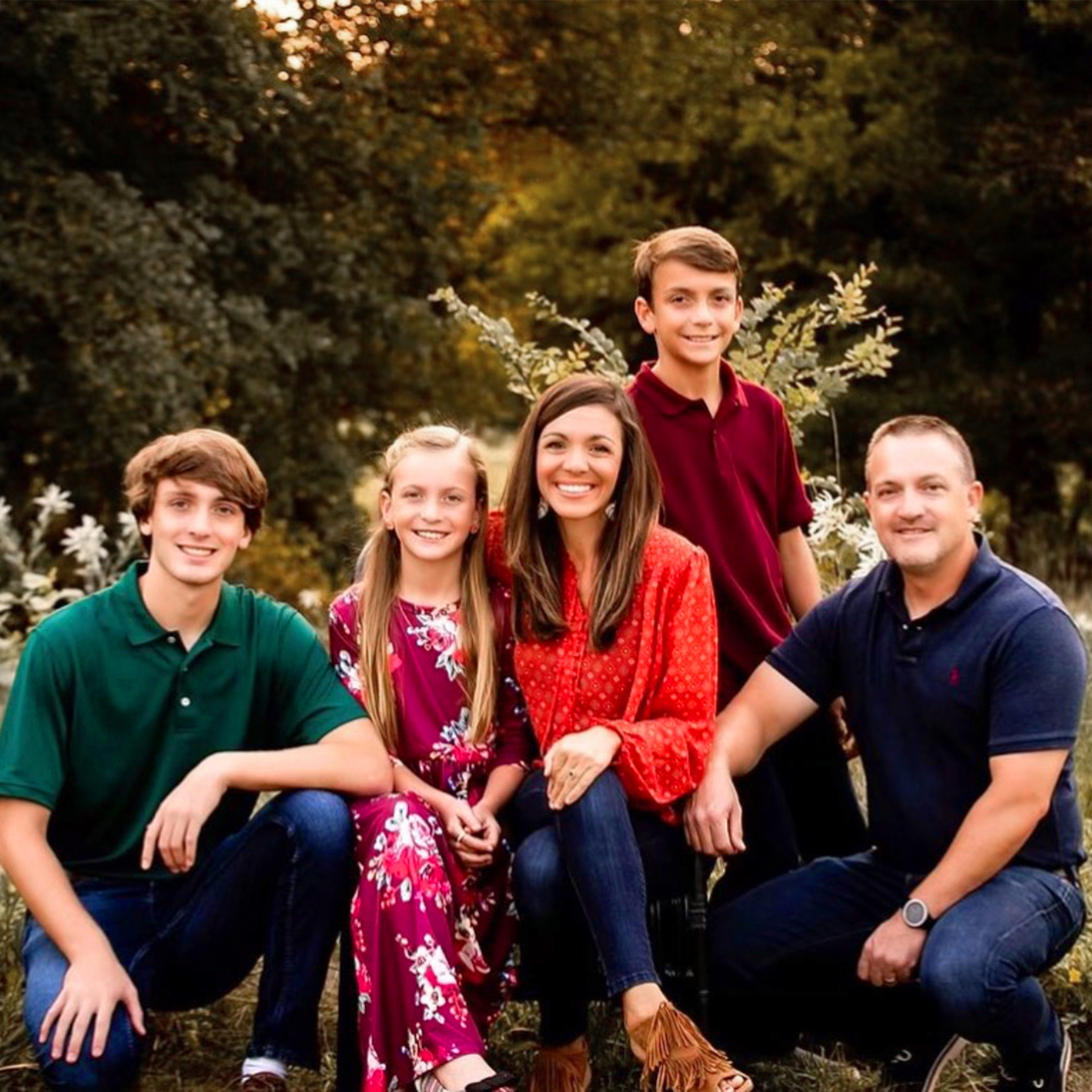 A family of five stand near greenery outdoors.