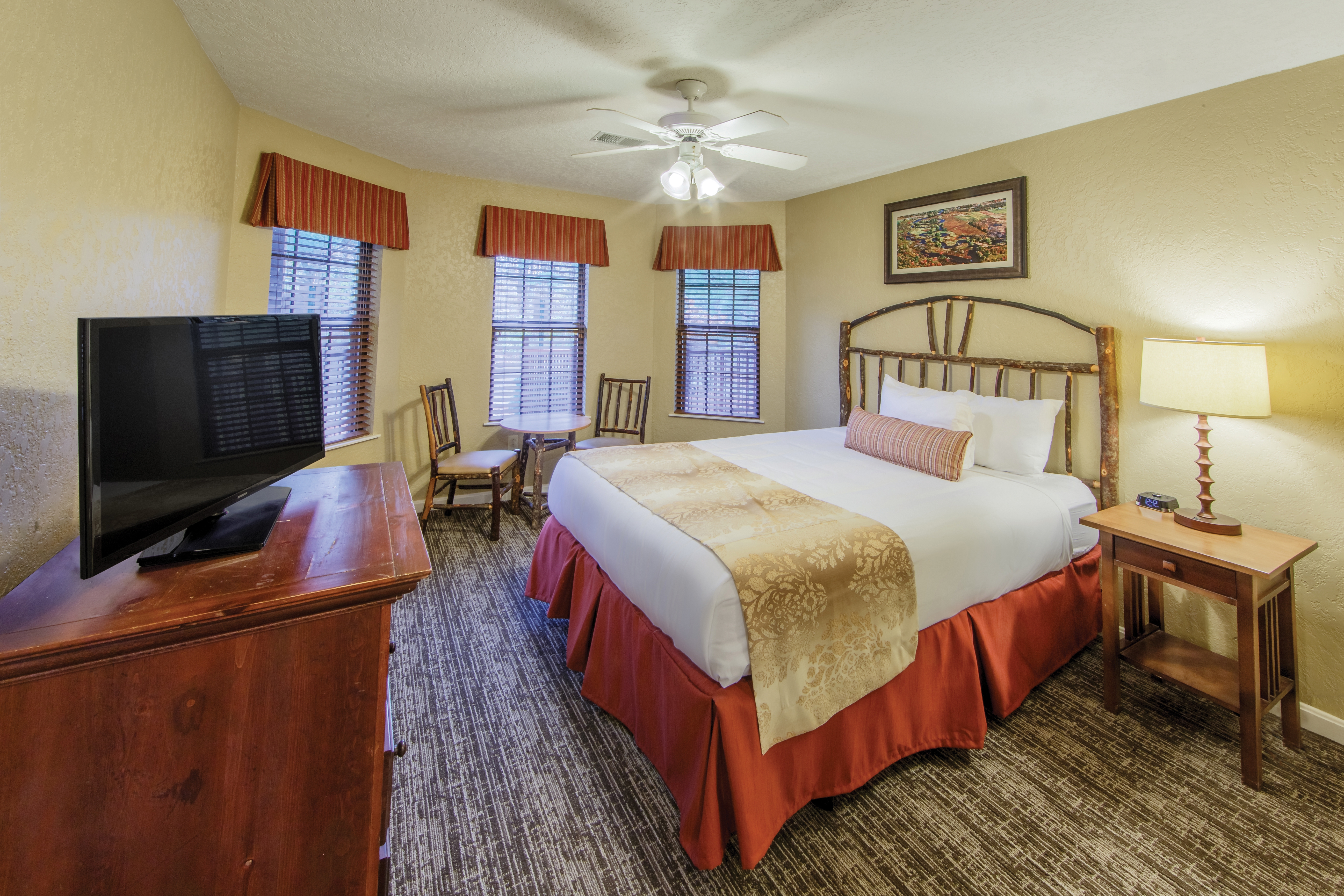Bedroom with three windows, sitting area, and tv in a two bedroom villa at Oak n' Spruce Resort in South Lee, Massachusetts