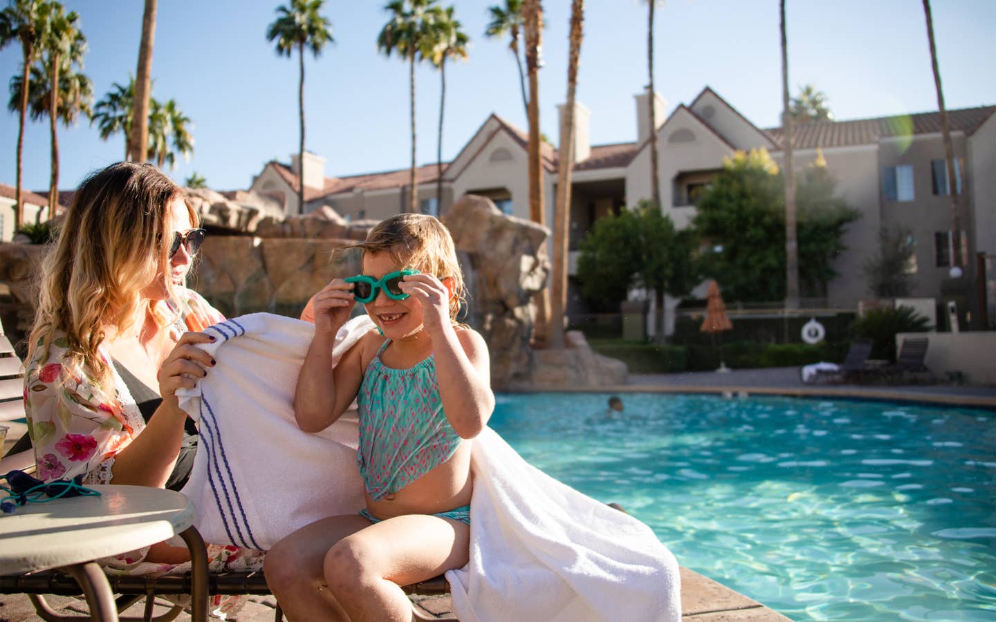 Mother and daughter sitting next to a resort pool and wearing sunglasses