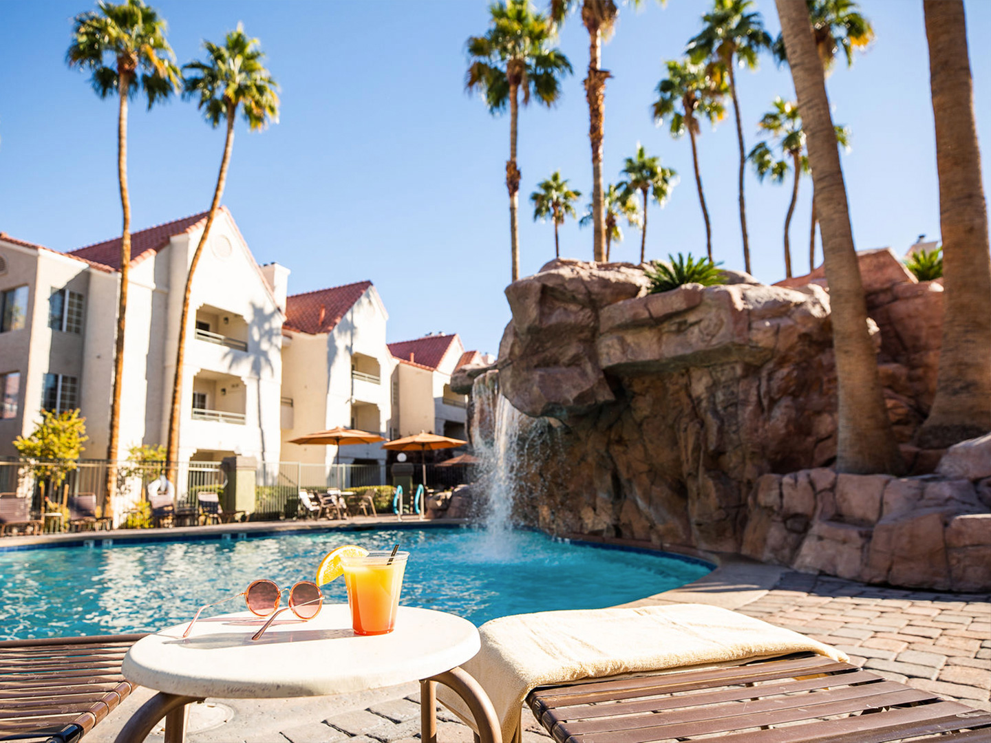 Table with sunglasses and fruity drink near outdoor pool at Desert Club Resort in Las Vegas, Nevada.