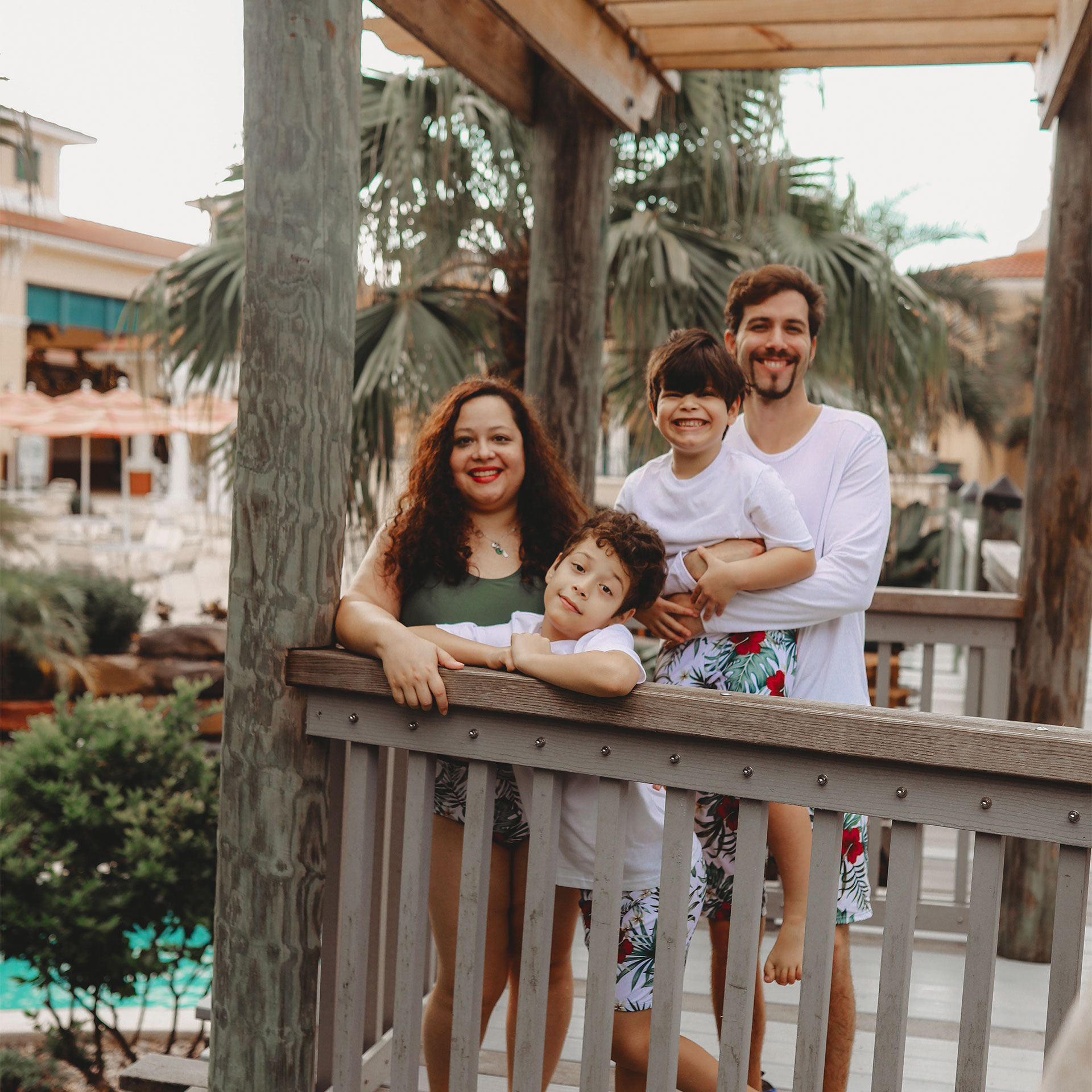 A woman, man and two young boys wear swimwear on a wooden patio.