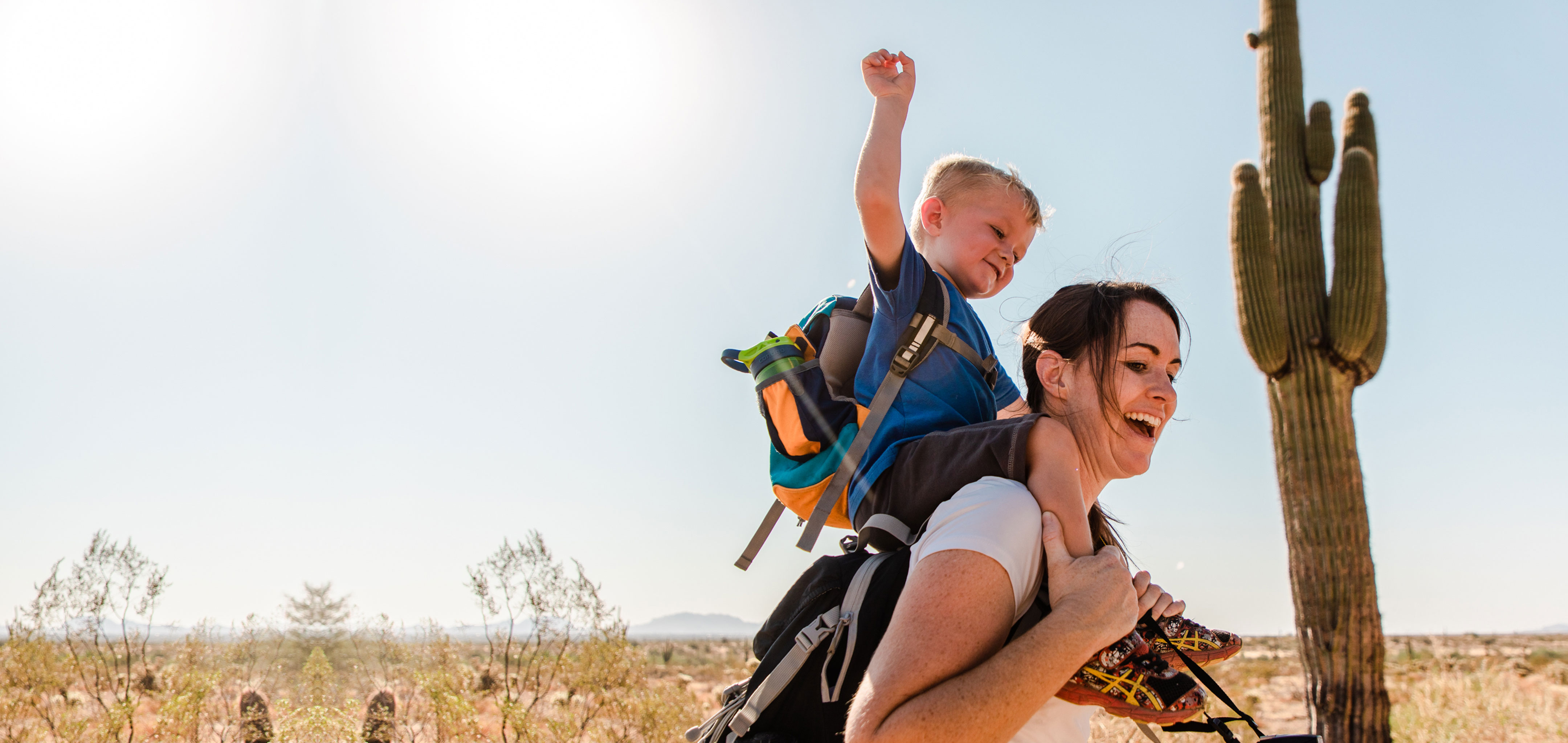 Jessica and her son laughing together while he sits on her shoulders as they hike in the Arizona desert.