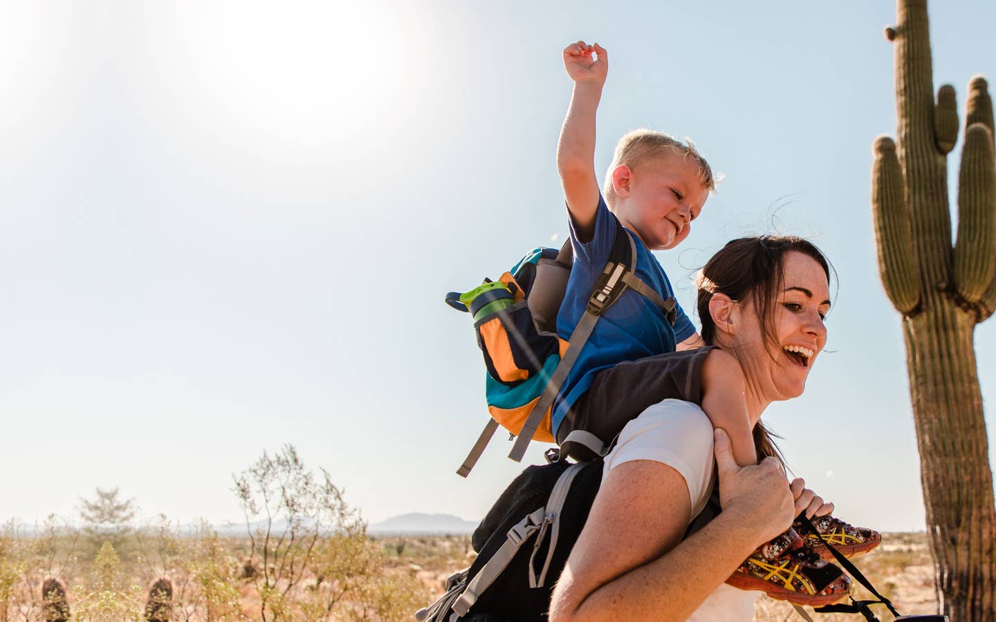 Jessica and her son laughing together while he sits on her shoulders as they hike in the Arizona desert.