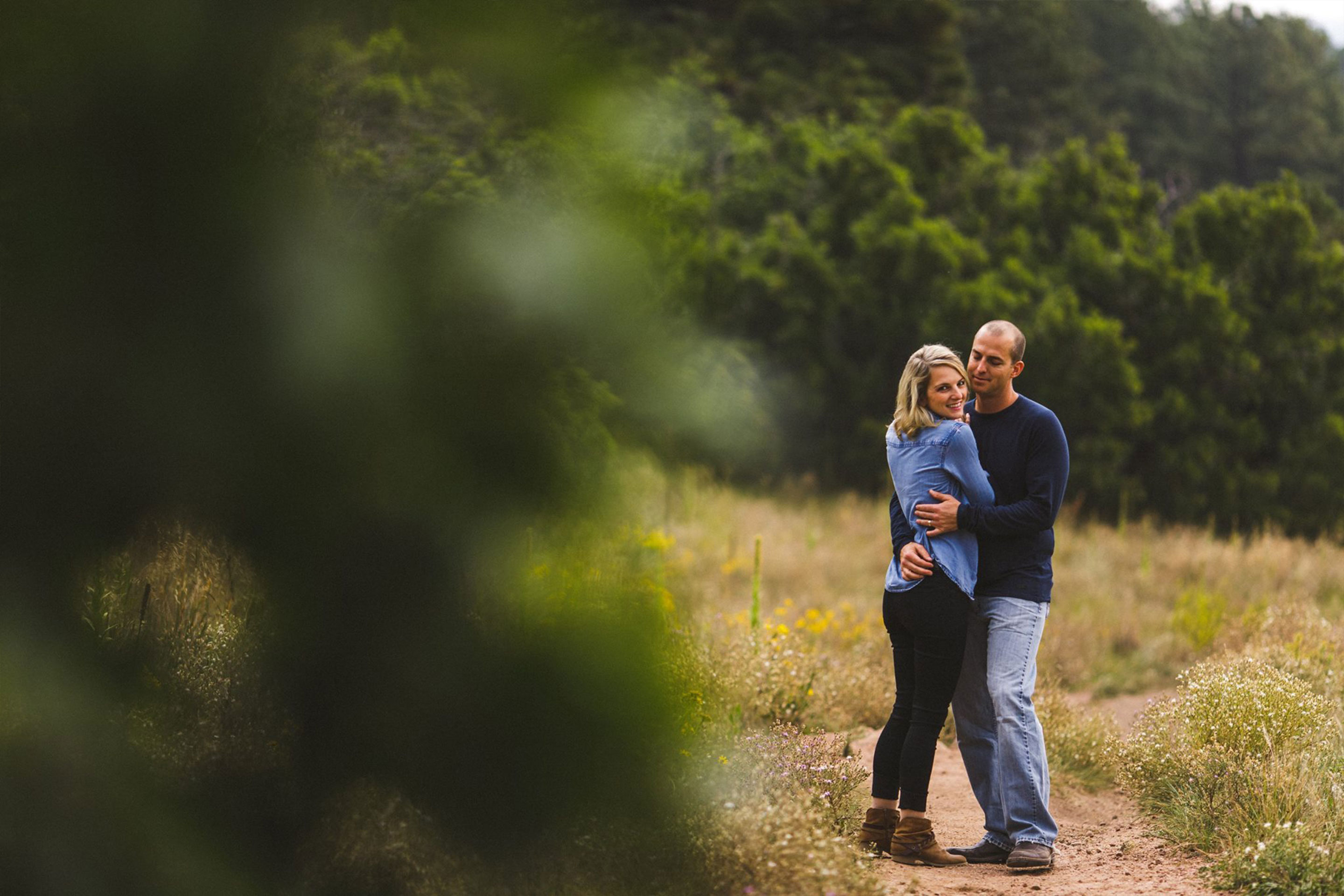 A couple stands outdoors holding embracing each other surrounded by a lush environment.