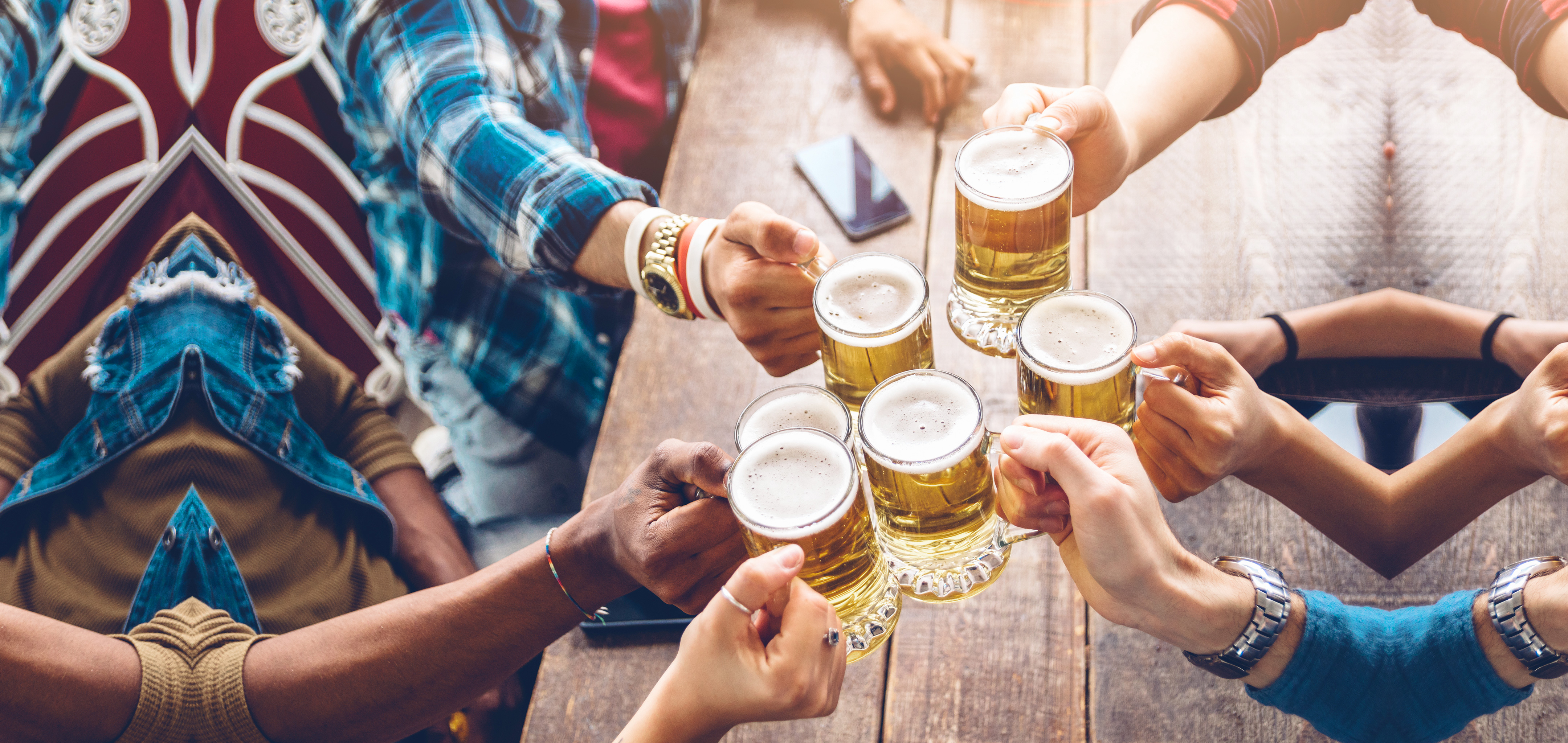 Several people hold their glasses of beer over a table giving 'cheers' to each other.