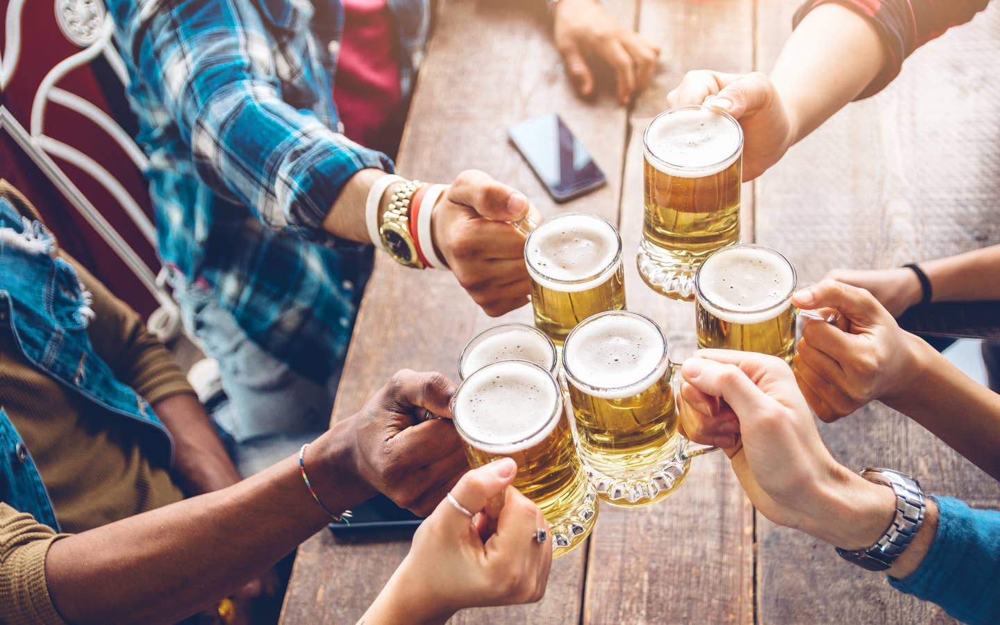 Several people hold their glasses of beer over a table giving 'cheers' to each other.