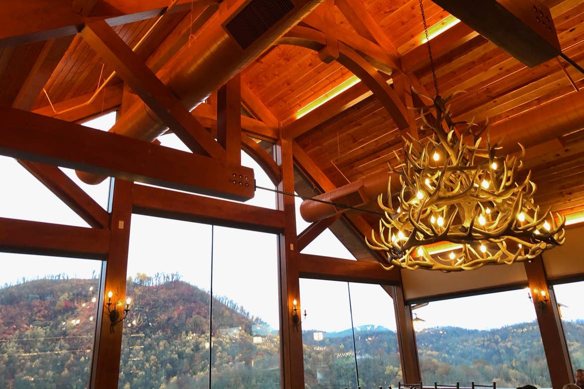 The interior of Anakeesta’s Cliff Top restaurant with a view of the mountain range, antler chandelier, and log architecture.