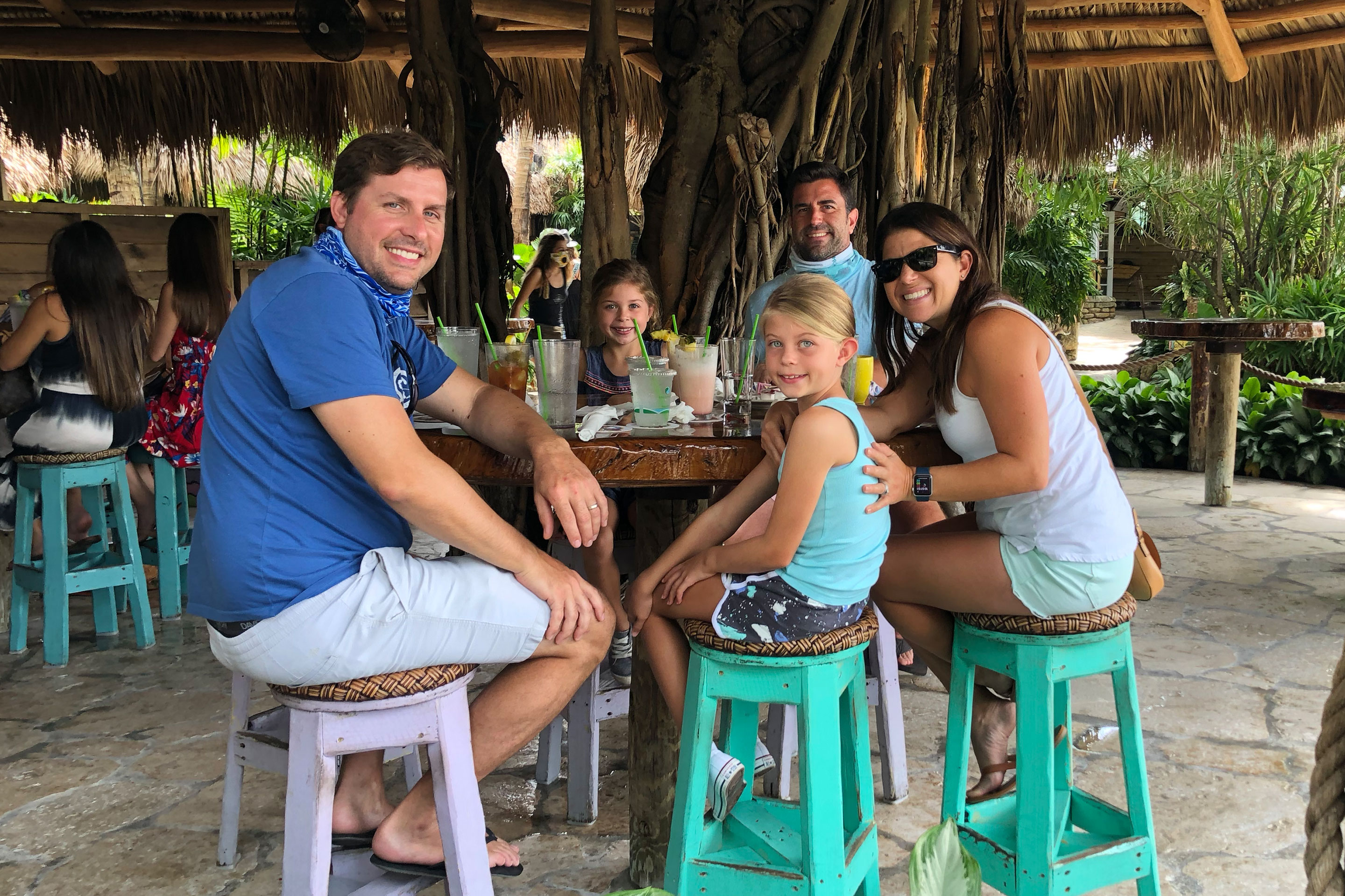 Featured Contributor, Chris Johnston (far-right), sits with her husband, Josh (back-right), and two daughters, Kyler (middle-left) and Kyndall (front-right), and family friend, Anthony (left), at a tiki-inspired dining table.