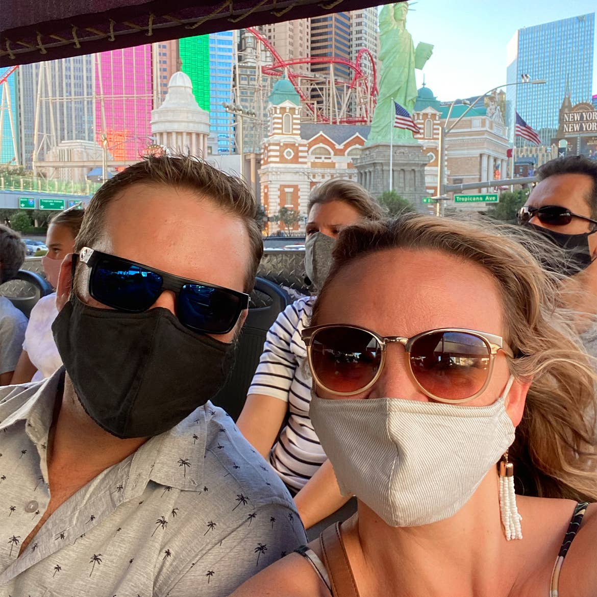 A woman wearing sunglasses and a face mask (right) poses near a man wearing sunglasses and a face mask (left) while seated on a double-decker bus tour near the Las Vegas Strip.