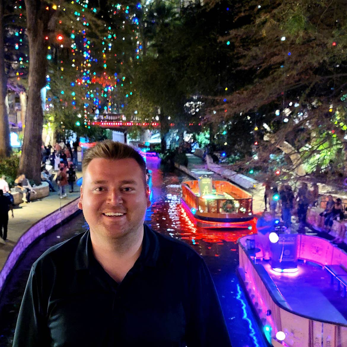 Author, Chris Harms, stands with in front of the San Antonio Riverwalk decorated for the holidays.