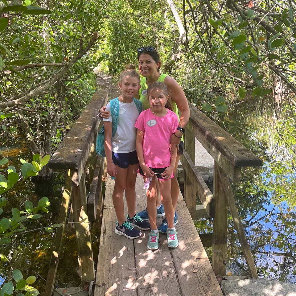 A caucasian woman (middle) poses with two young caucasian girls (front) on a wooden bridge in the Everglades.
