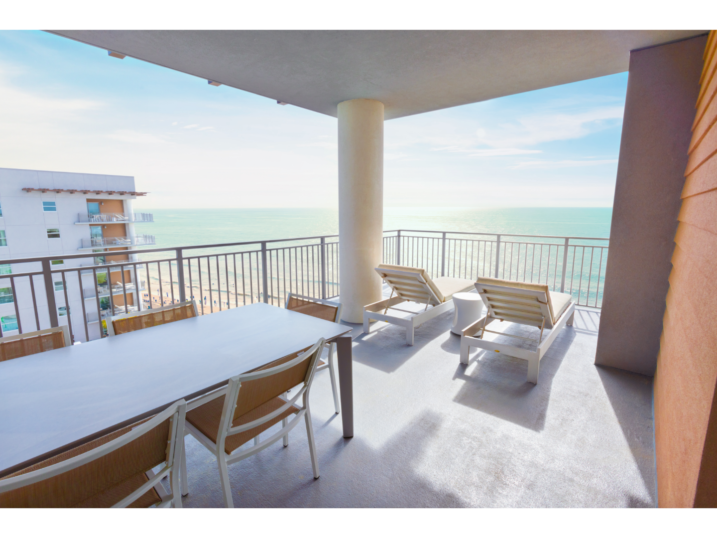 Lounge chairs on hotel balcony overlooking bright blue ocean.