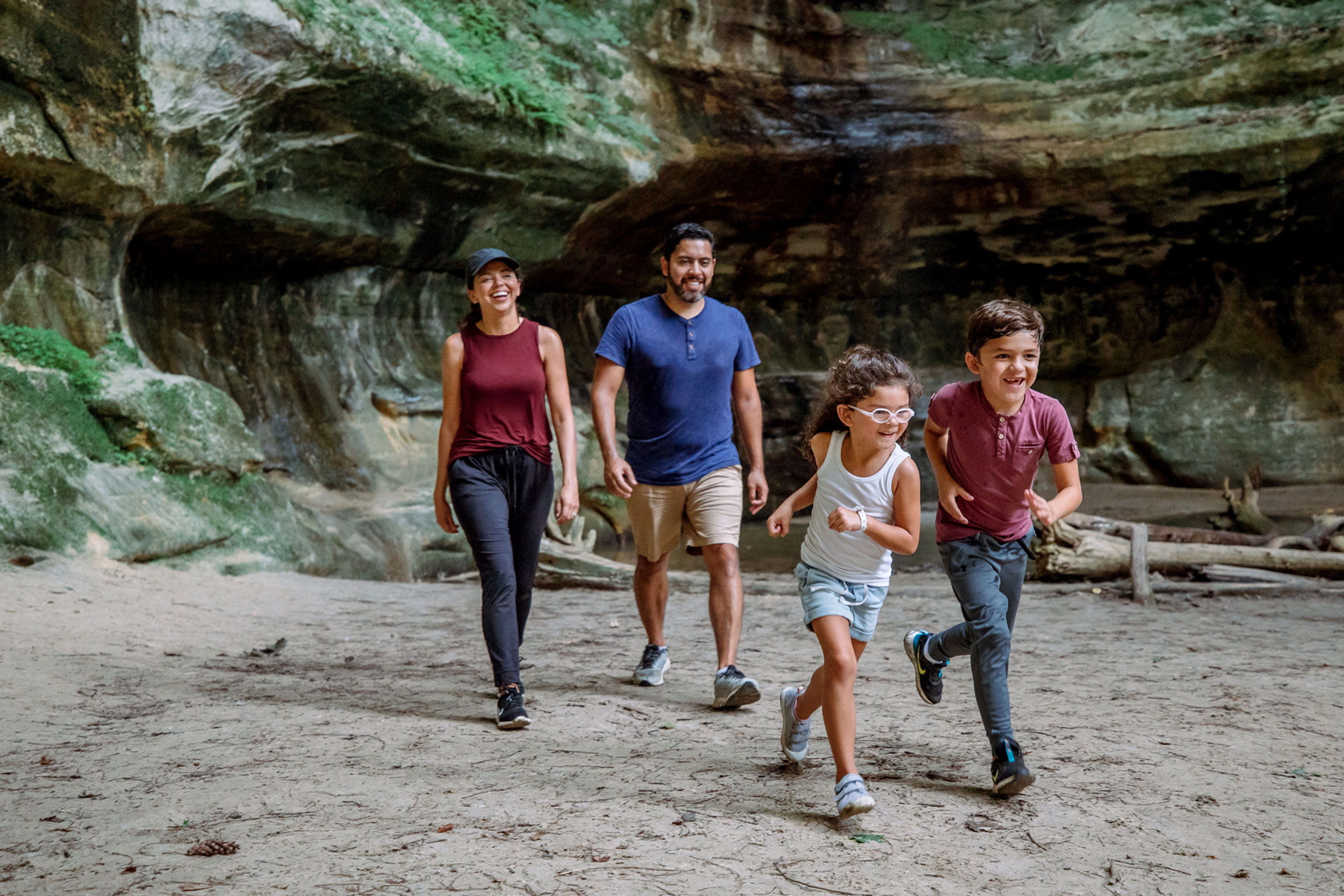 A family of four, one woman, a man, and a young boy and girl, walk outdoors on rocky terrain.