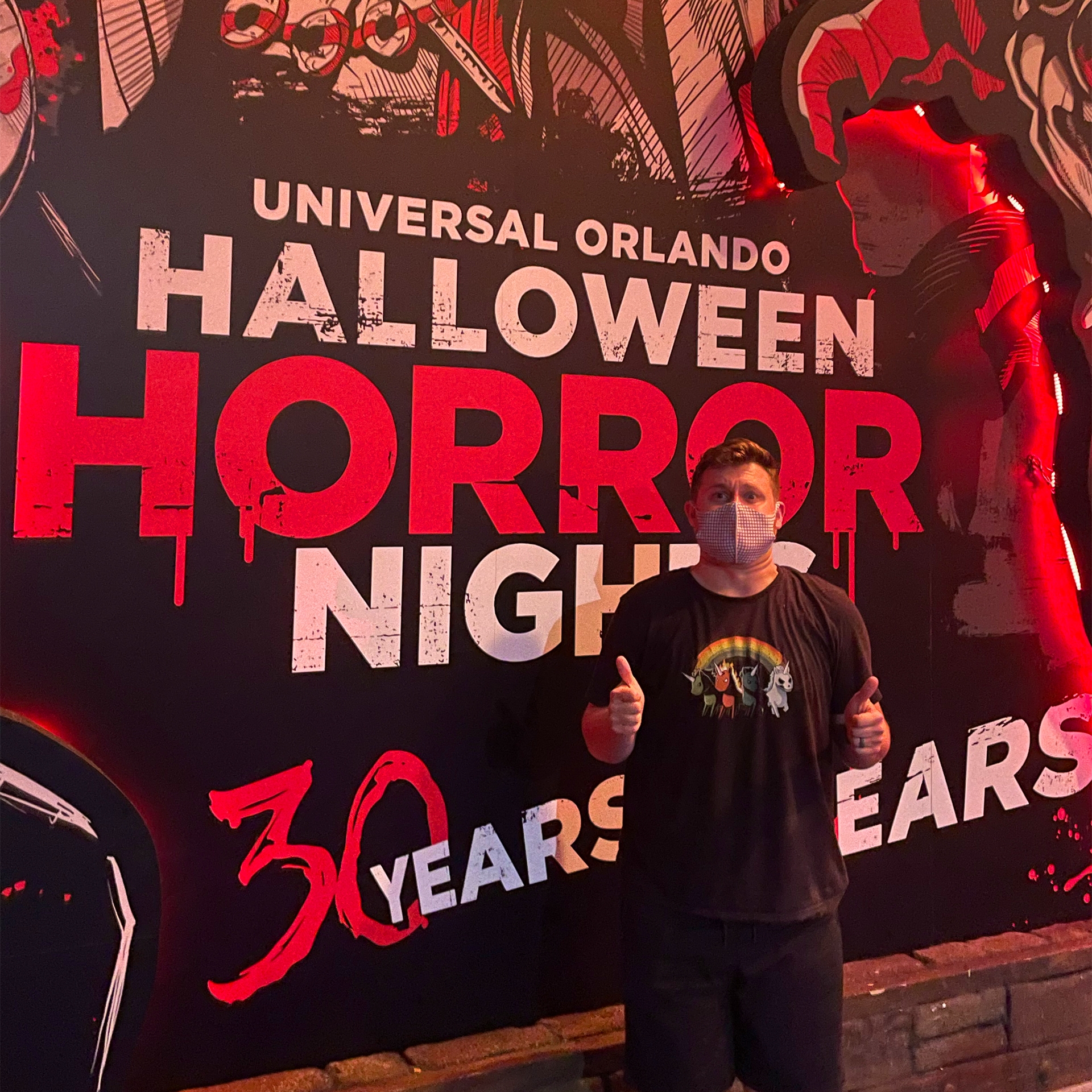 A male wearing black t-shirt and shorts stands in front of a Halloween mural.