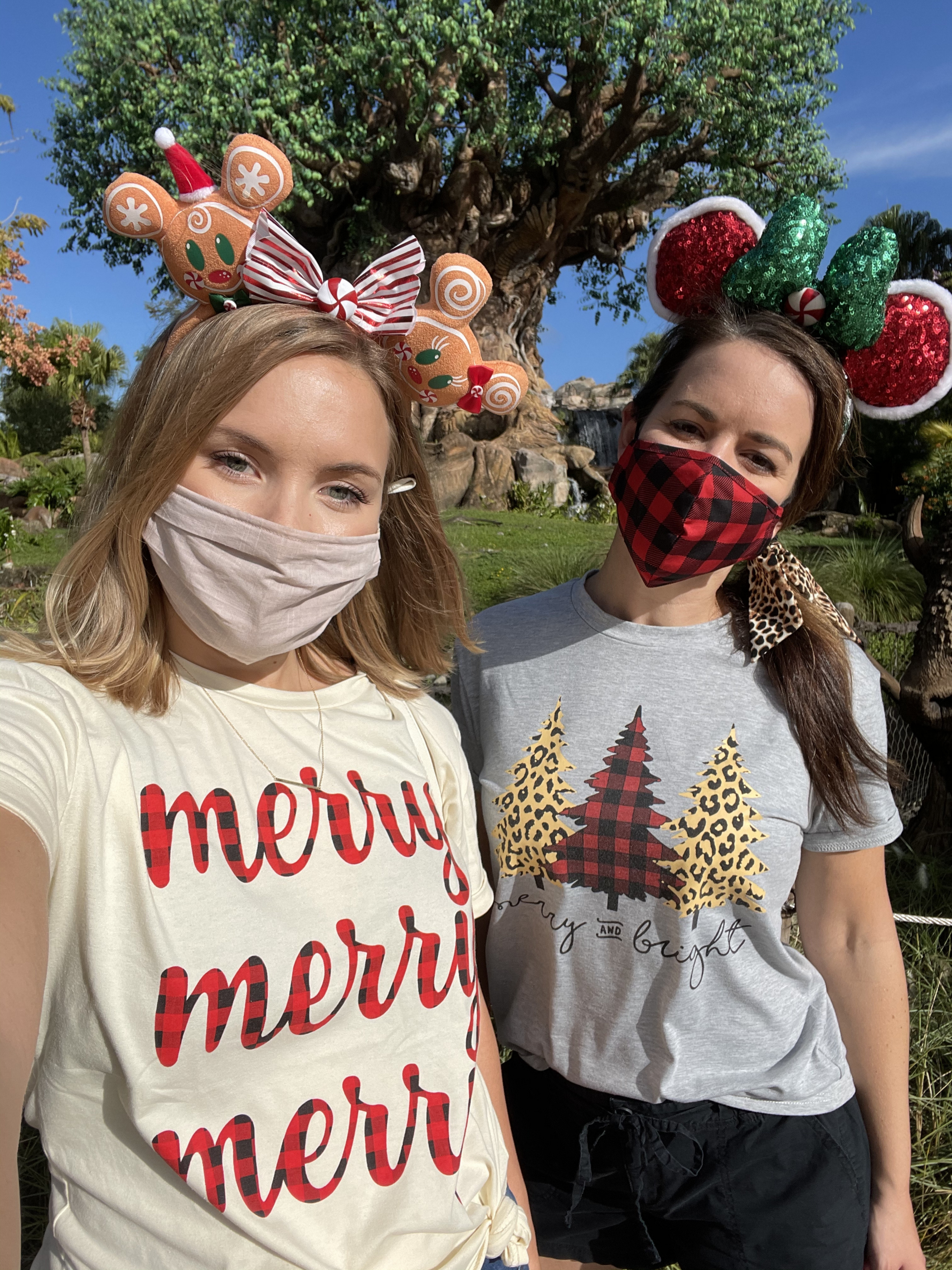 Author, Kelly Nelson (left), and Jenn C. Harmon (right) wear holiday inspired shirts and Minnie Mouse Ears within front of the Christmas Tree at Disney's Animal Kingdom Theme Park at Walt Disney World® Resort.