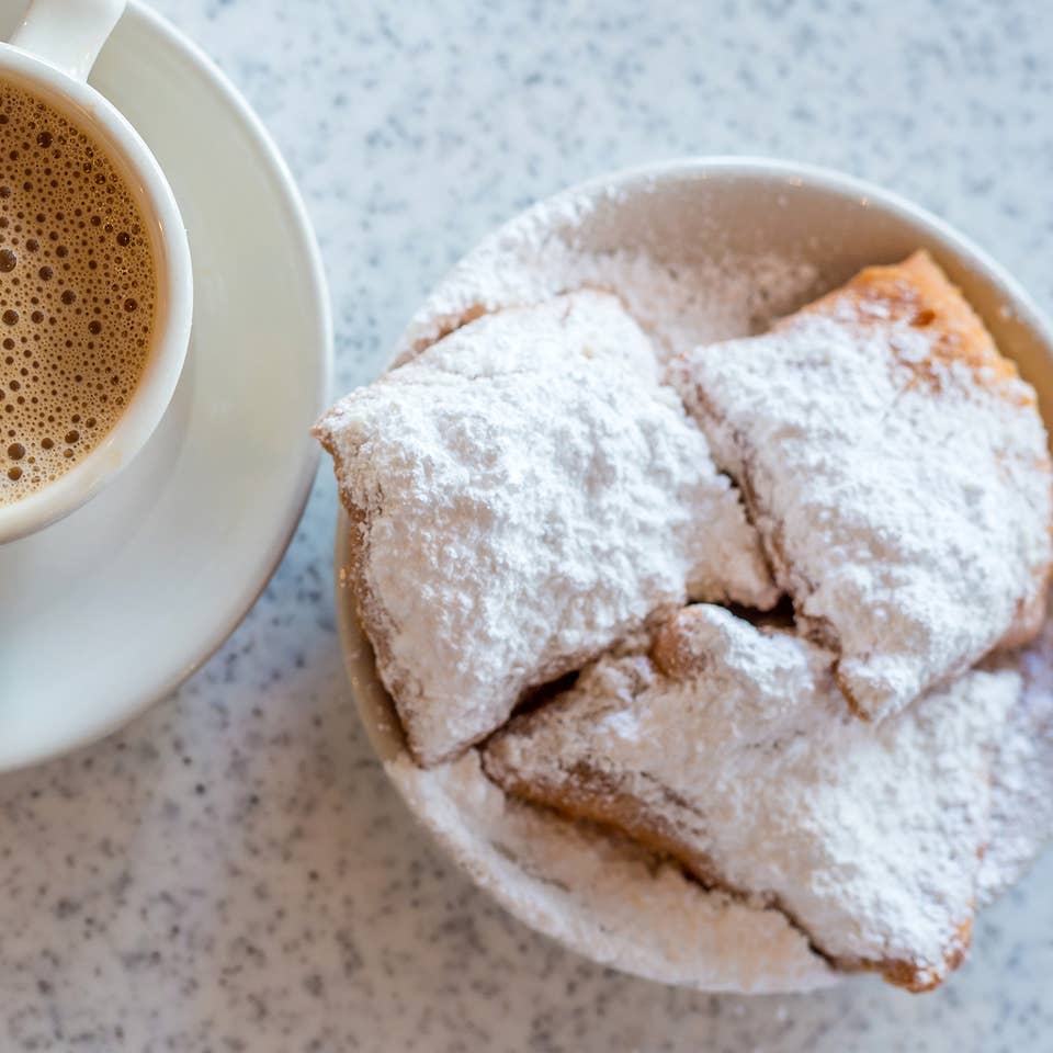 Beignets placed on a table with some coffee on white plates.