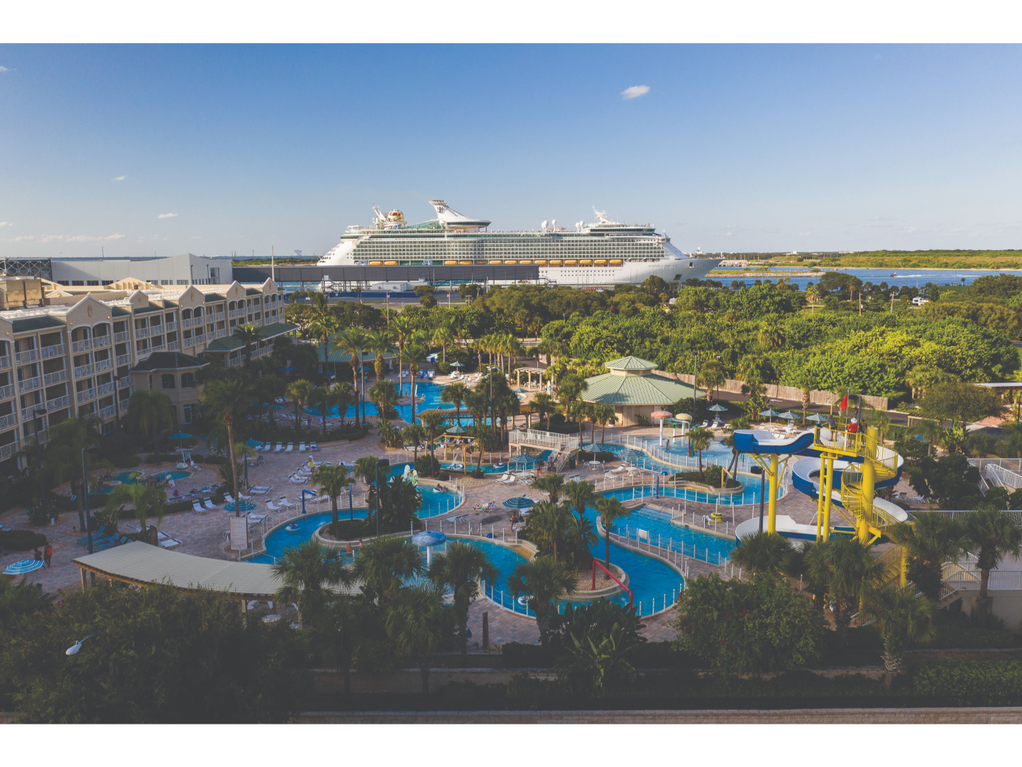 Aerial view of resort featuring multiple pools and waterslides, with a large cruise ship docked in the background.