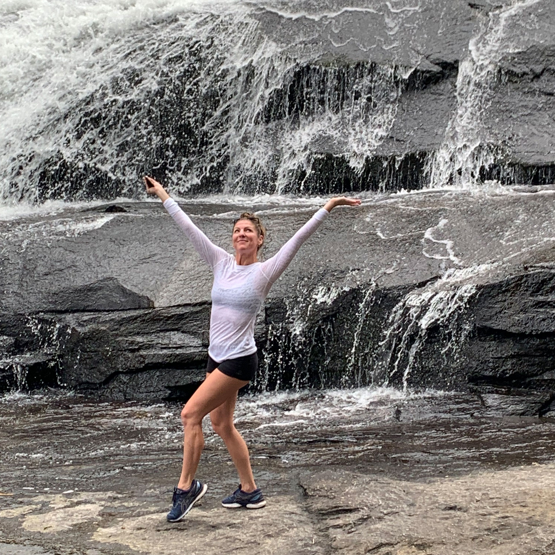 Co-author, Christine, wears a white shirt and black shorts while posing in front of a waterfall.