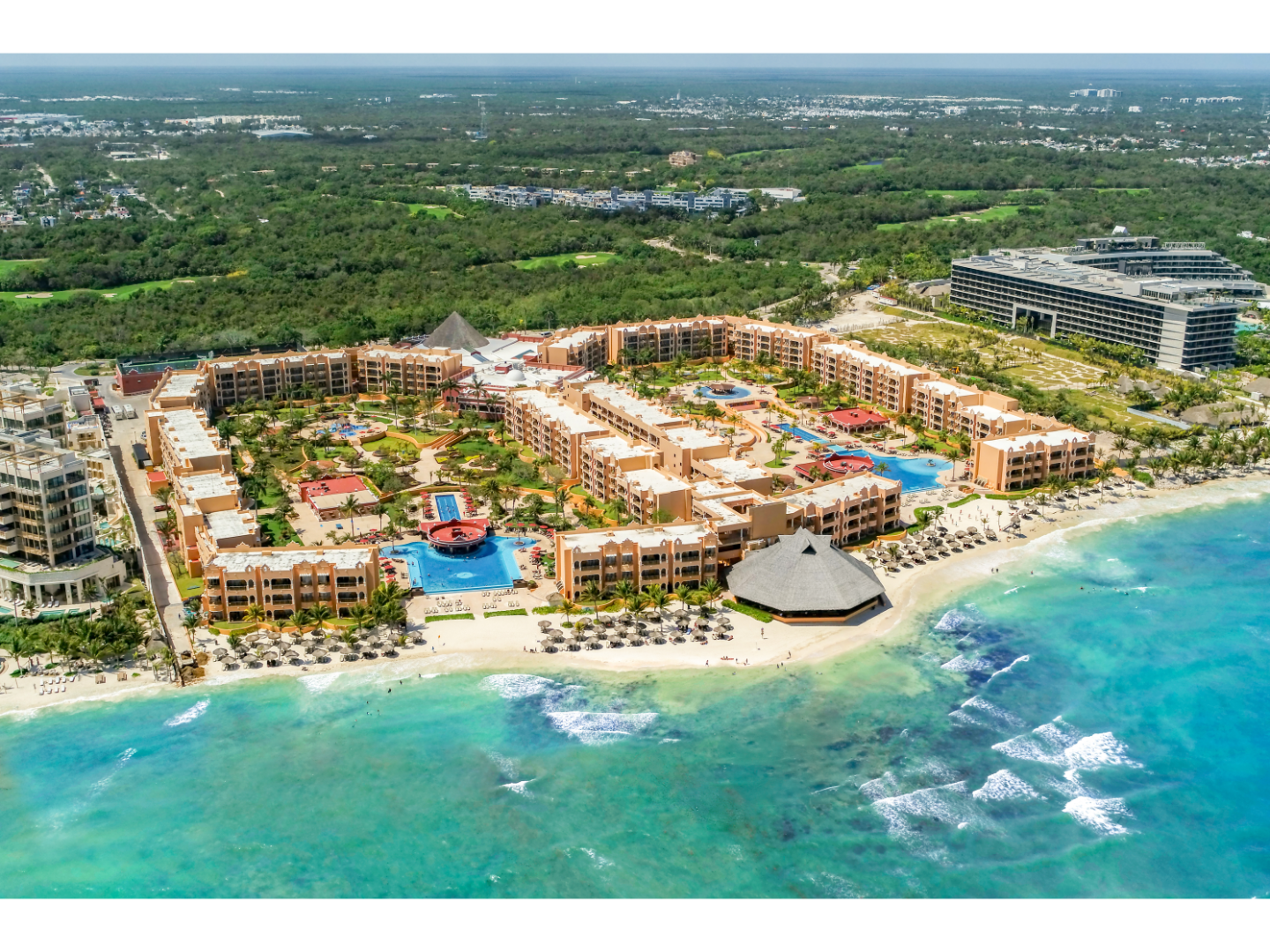 Aerial view of beachfront resort with pools and lush green surroundings.