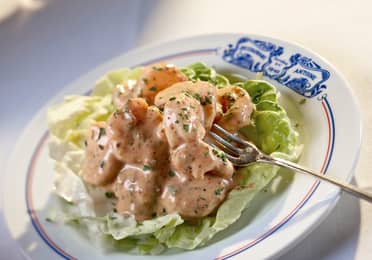 A white plate with blue toile imprint that reads 'Antoines' containing shrimp in Antoine's rémoulade.